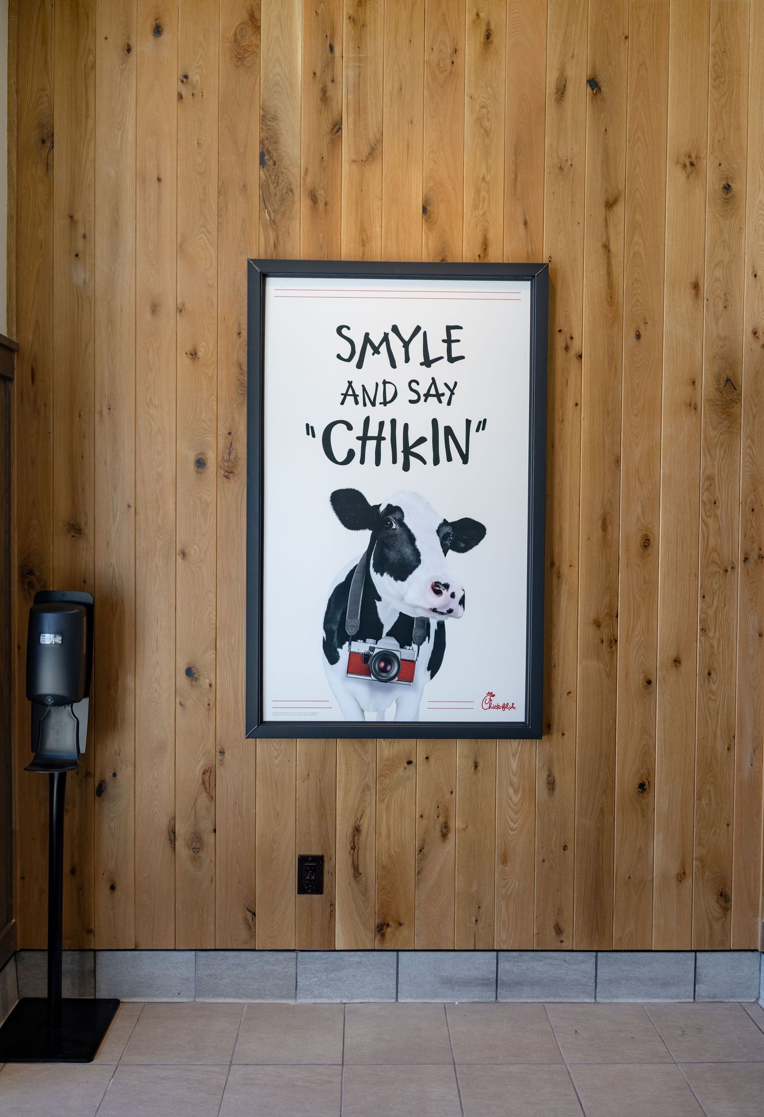 Framed Chick-fil-A cow poster reading Smyle and Say Chikin on a wooden wall.