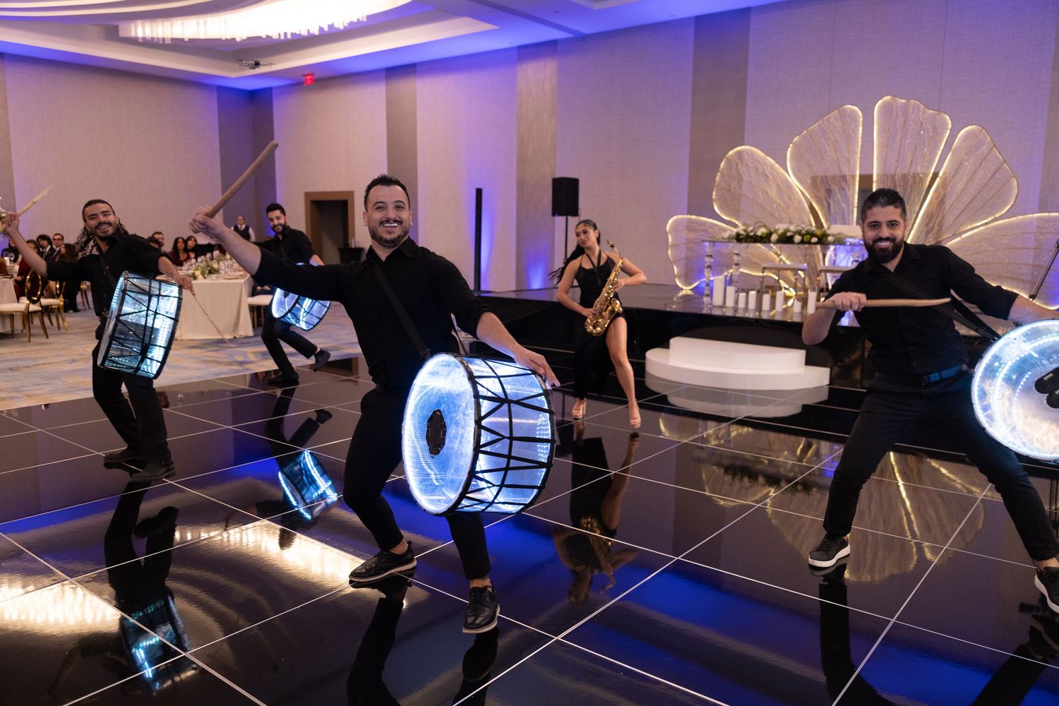 Performers in black outfits playing illuminated drums on a dance floor at an elegant event venue.