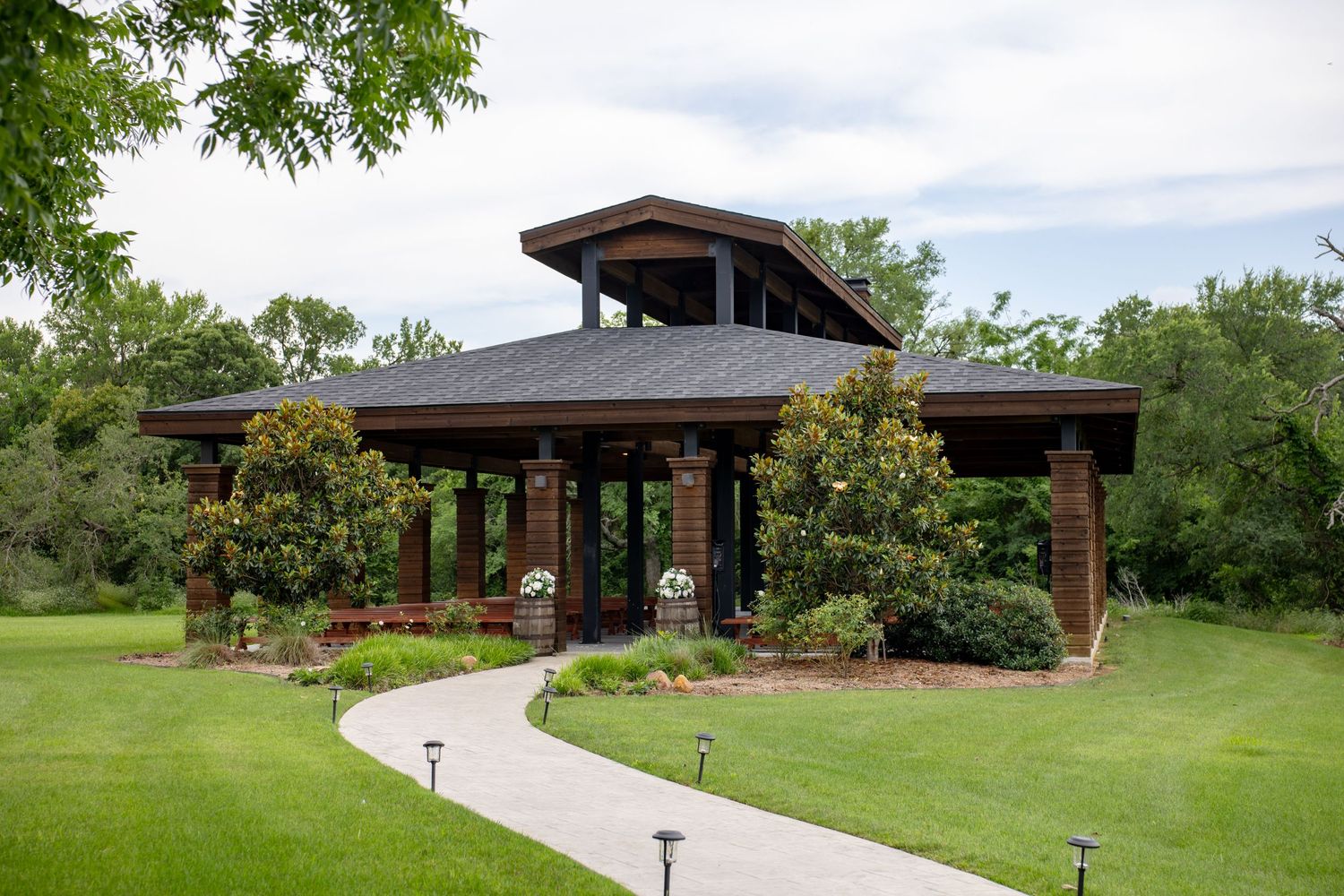 Elegant outdoor wedding ceremony pavilion with brick columns surrounded by lush green landscaping and pathway.