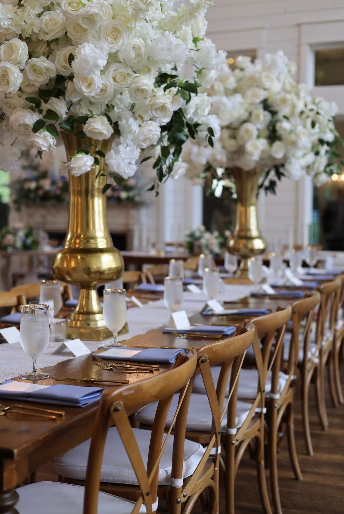 Elegant reception tables with tall white rose arrangements in gold vases and navy napkins.