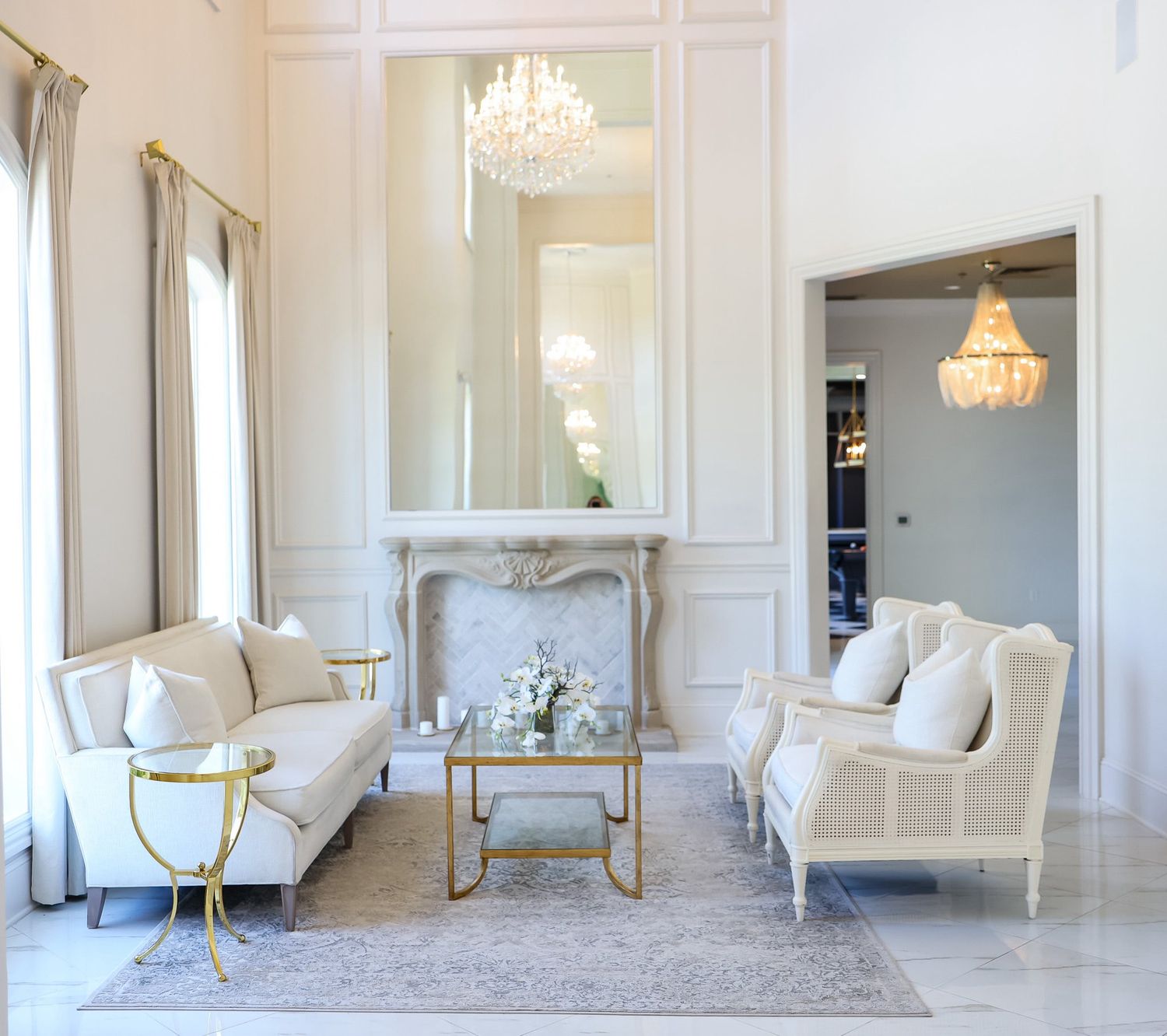 Elegant white sitting room with crystal chandelier, marble fireplace, and white sofas.