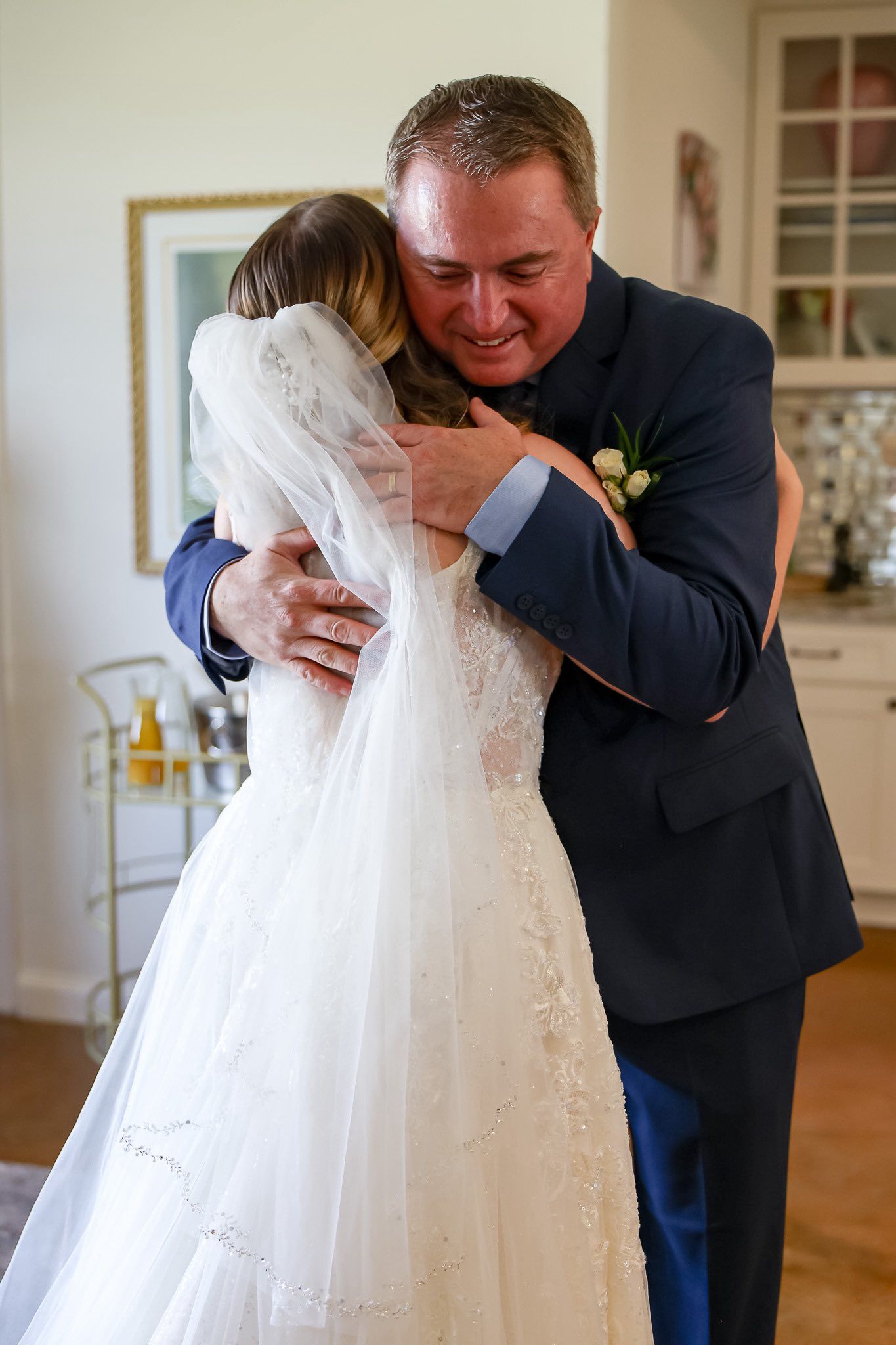 Father of the bride embracing his daughter in her white wedding gown and veil in an emotional first look moment.