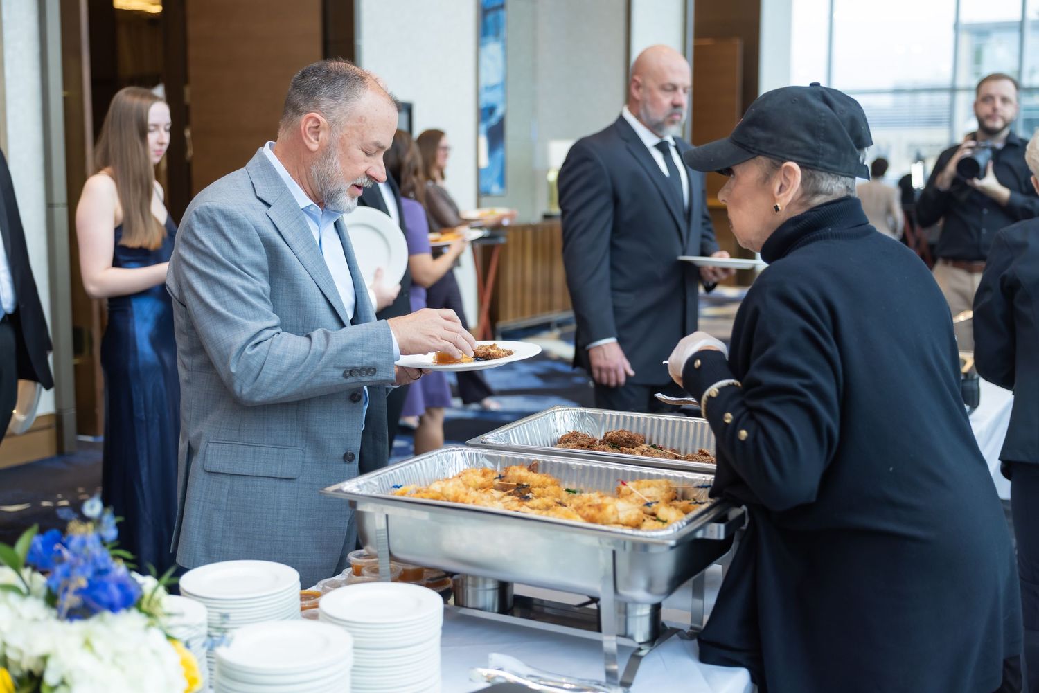 A man in a gray suit serves himself food at a buffet catering station during a formal event.