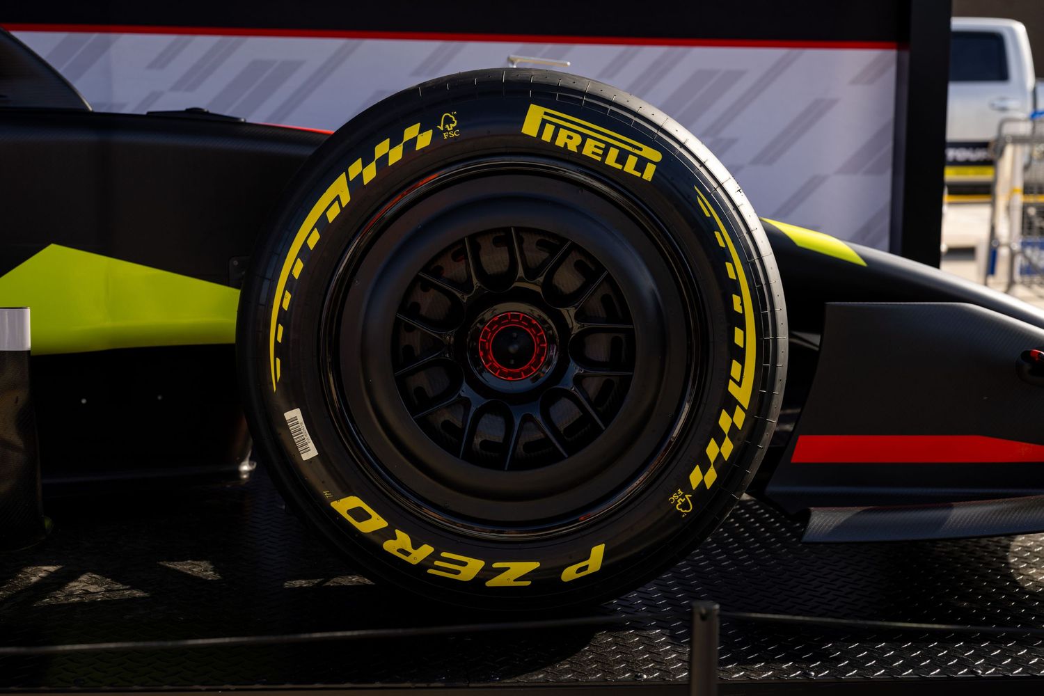 Close-up of a Pirelli P Zero yellow-marked Formula 1 racing tire on a black multi-spoke wheel of a green race car.