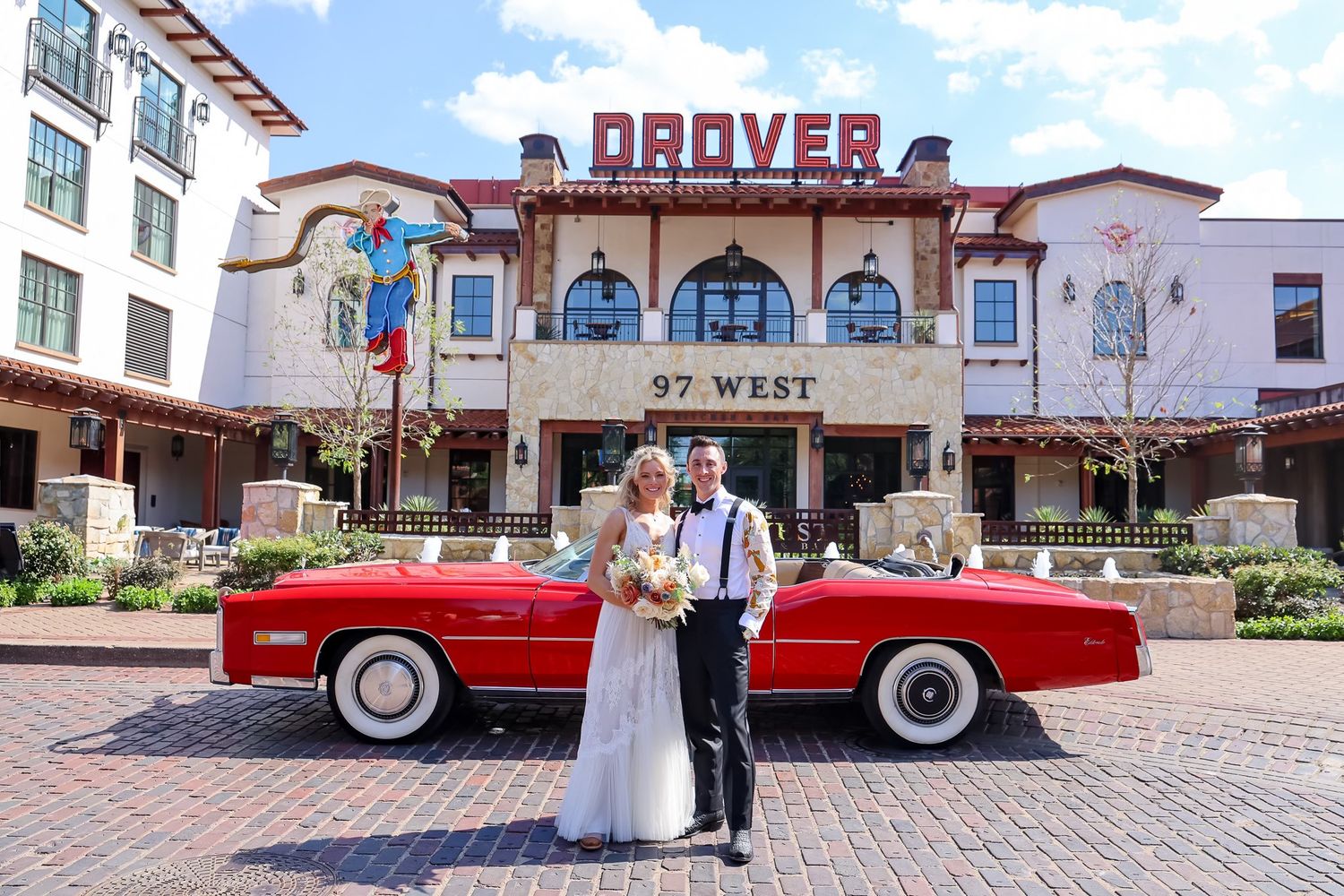 Bride and groom posing in front of a classic red Cadillac convertible outside the Drover Hotel in Fort Worth.