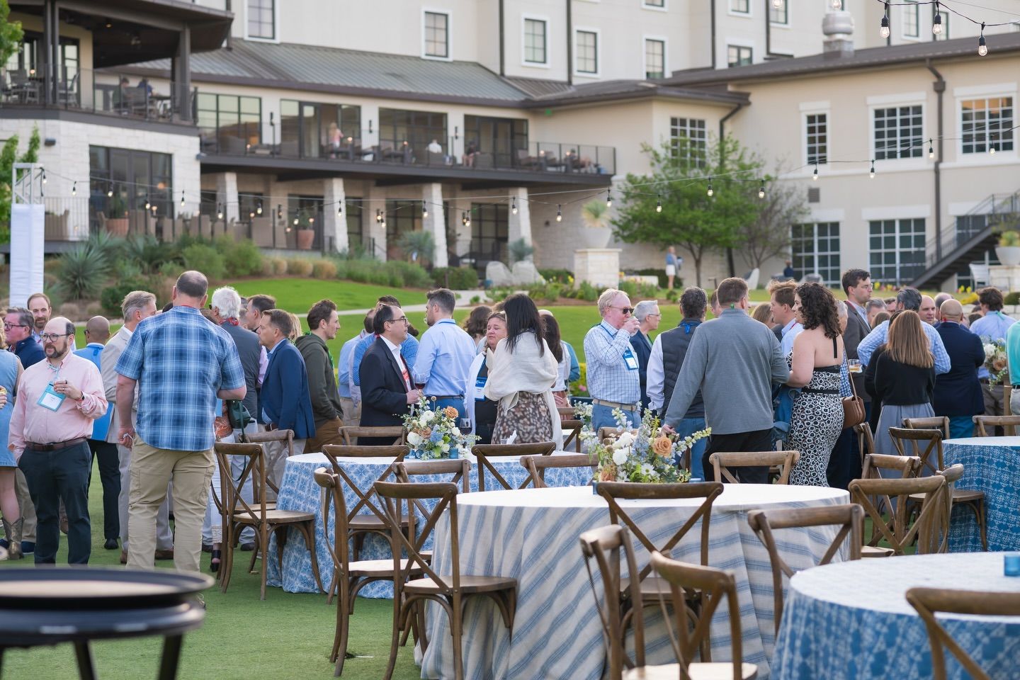 Guests mingling at an outdoor evening reception with blue tablecloths and floral centerpieces at the omni hotel resort in Austin TX.