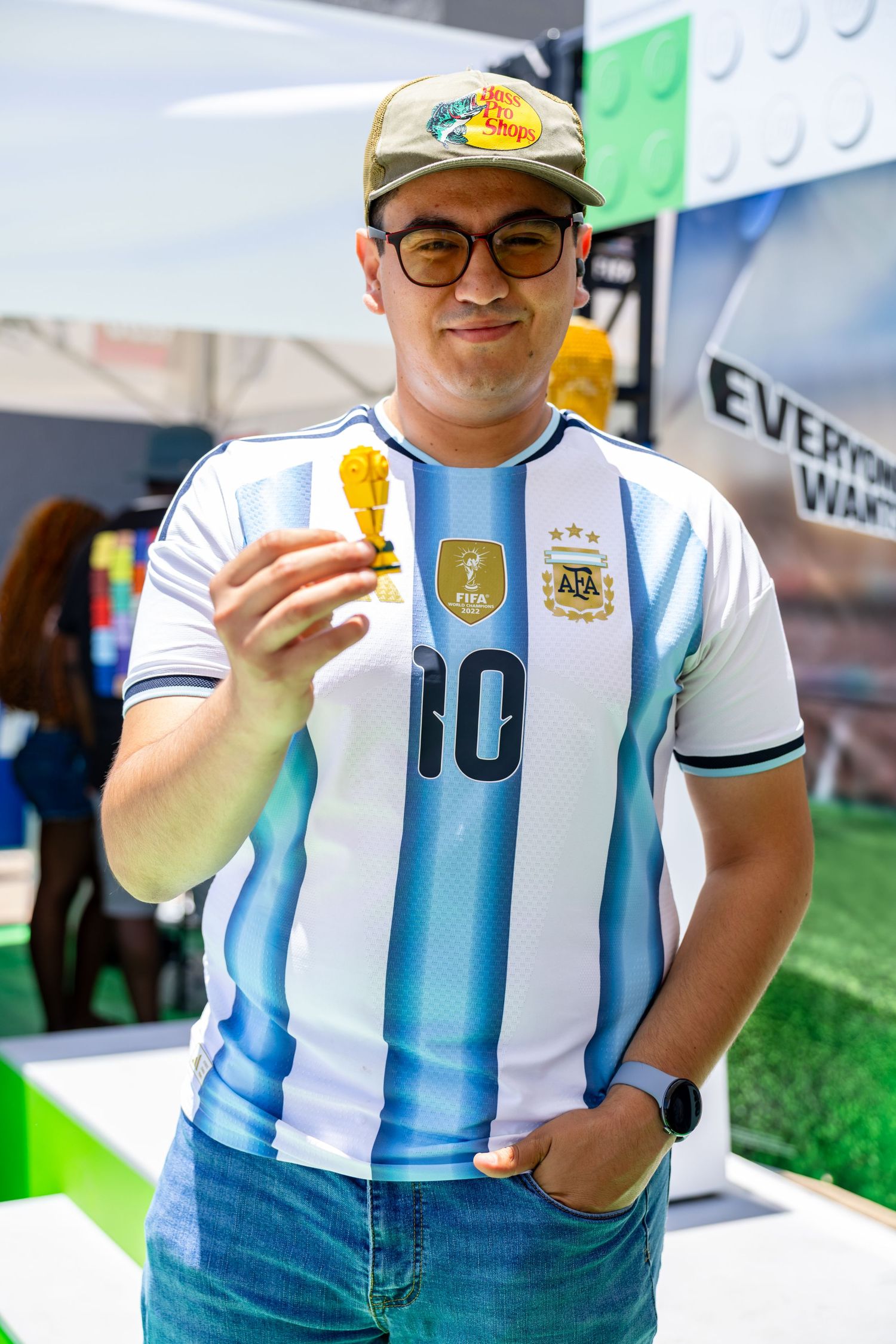 A man wearing an Argentina number 10 FIFA jersey holds a small golden World Cup trophy replica outdoors.