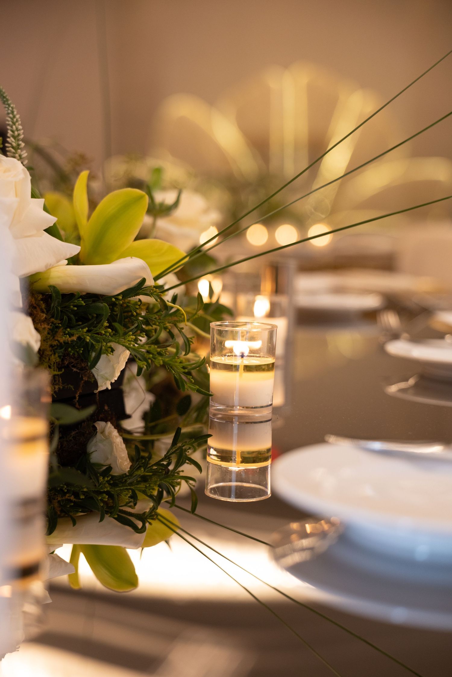 Elegant wedding table setting with floral centerpiece, white flowers, greenery, and glowing candles in glass holders.