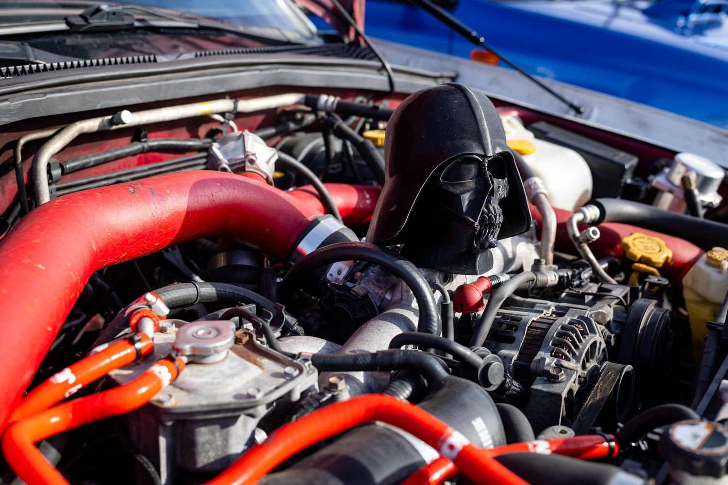 Close-up of a modified car engine with red turbo pipes and performance parts under an open hood.