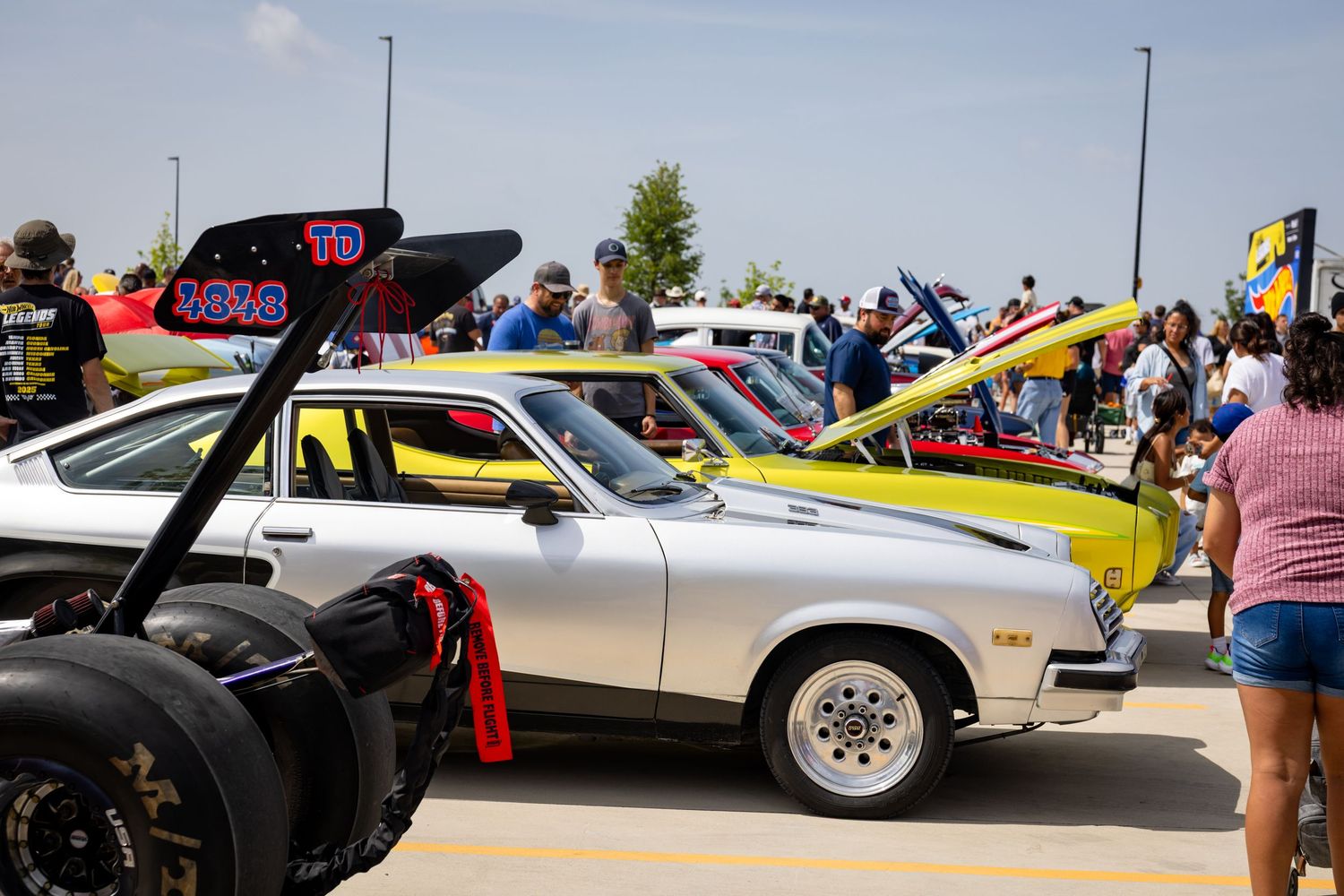Classic cars on display at an outdoor car show, featuring a silver muscle car surrounded by colorful vintage vehicles and spectators.