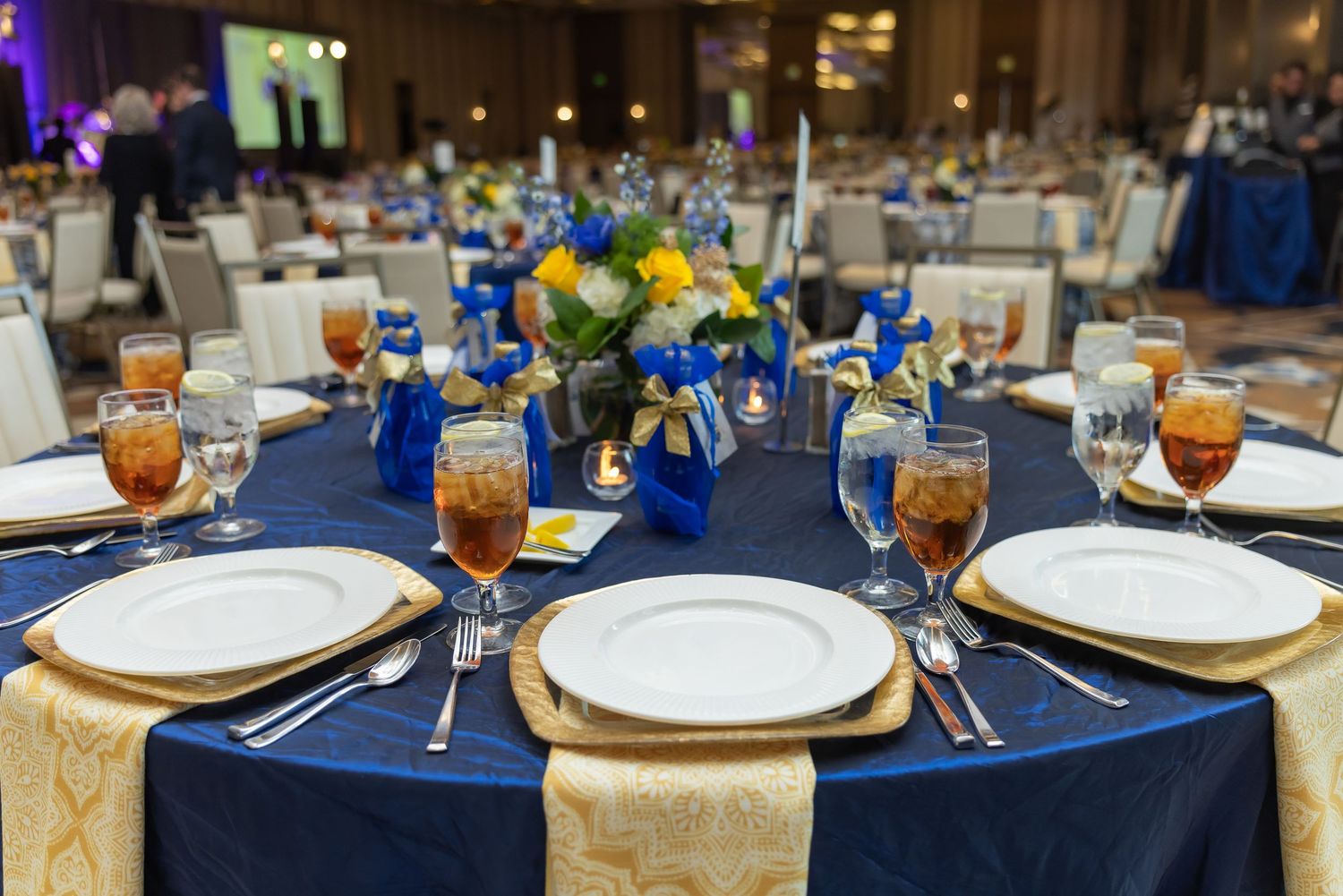 Elegant banquet table set with navy blue linens, gold chargers, and floral centerpieces. Gala at the omni hotel in frisco tx.