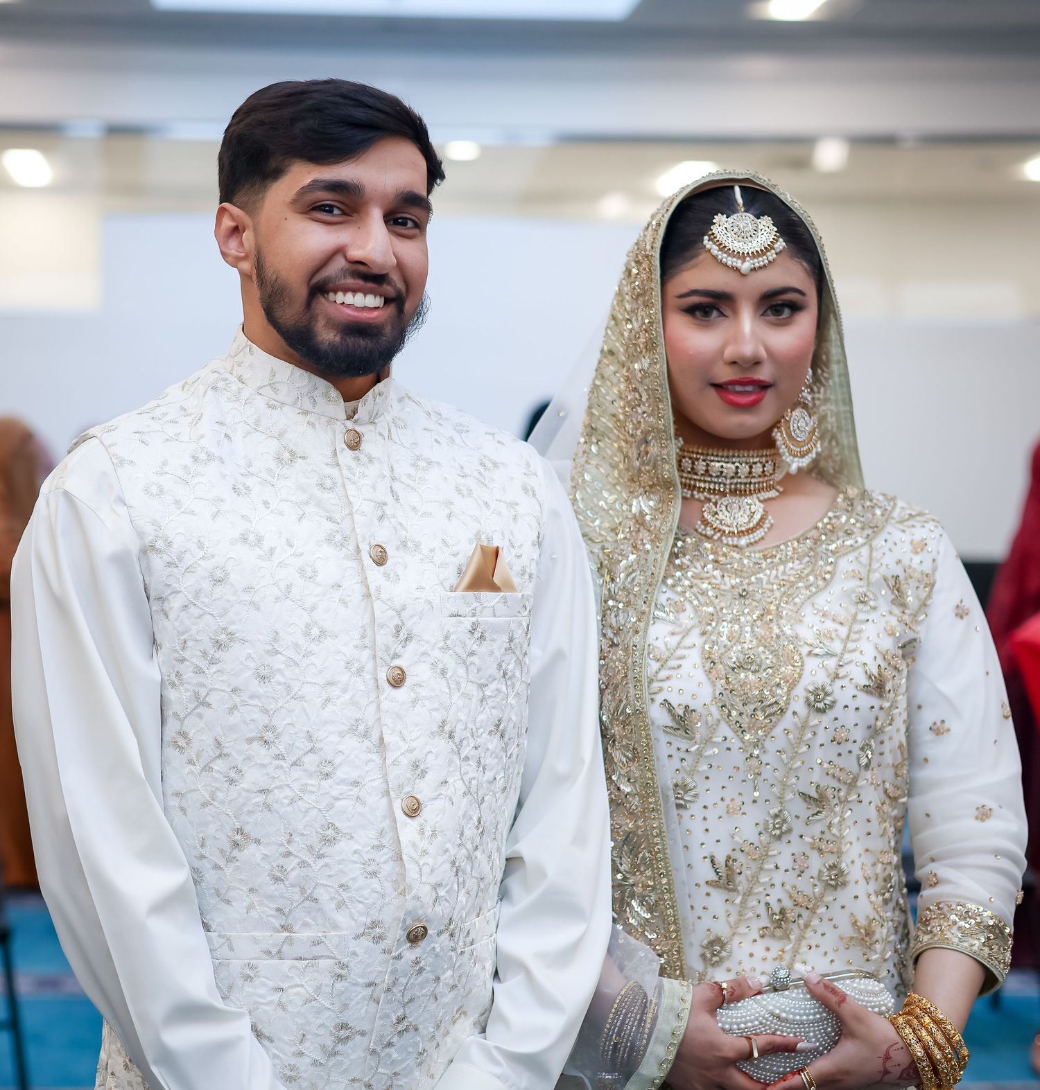 South Asian couple in traditional white and gold wedding attire smiling at their nikah ceremony.