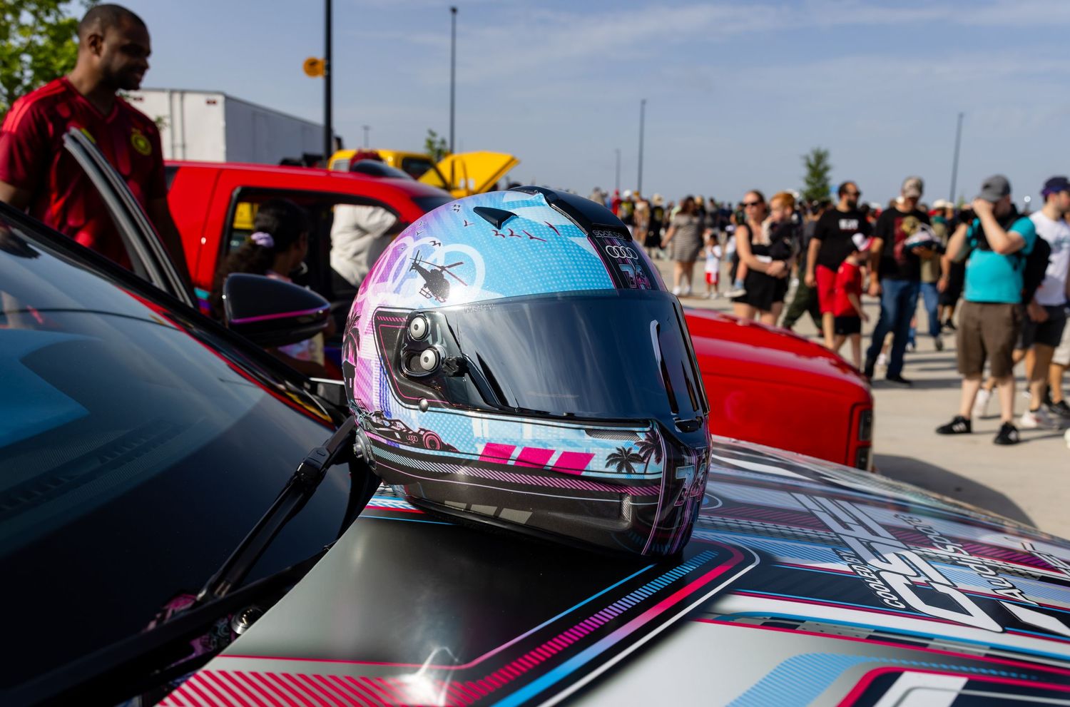 Colorful racing helmet with blue and pink design resting on a race car door at an automotive event.
