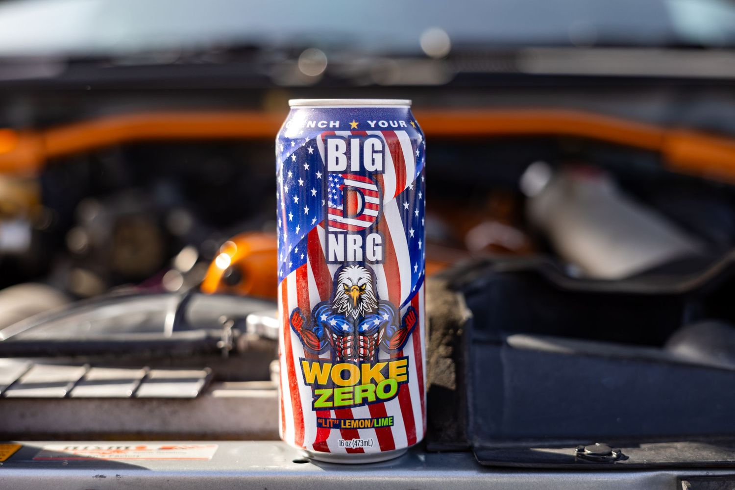 Big D NRG Woke Zero energy drink can with patriotic eagle design displayed near a vehicle engine.