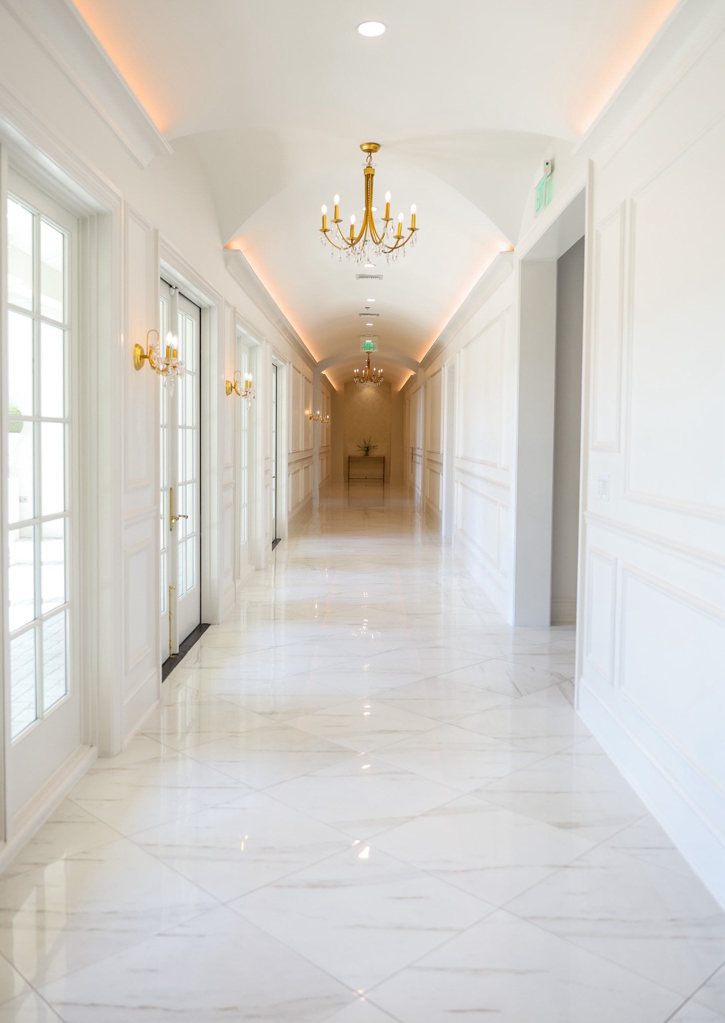 Bright white marble corridor with gold chandeliers, wall sconces, and arched ceiling.