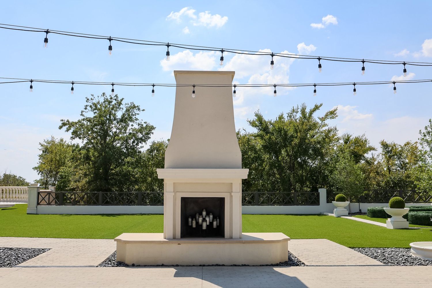 Outdoor white stone fireplace with string lights and manicured lawn at event venue.