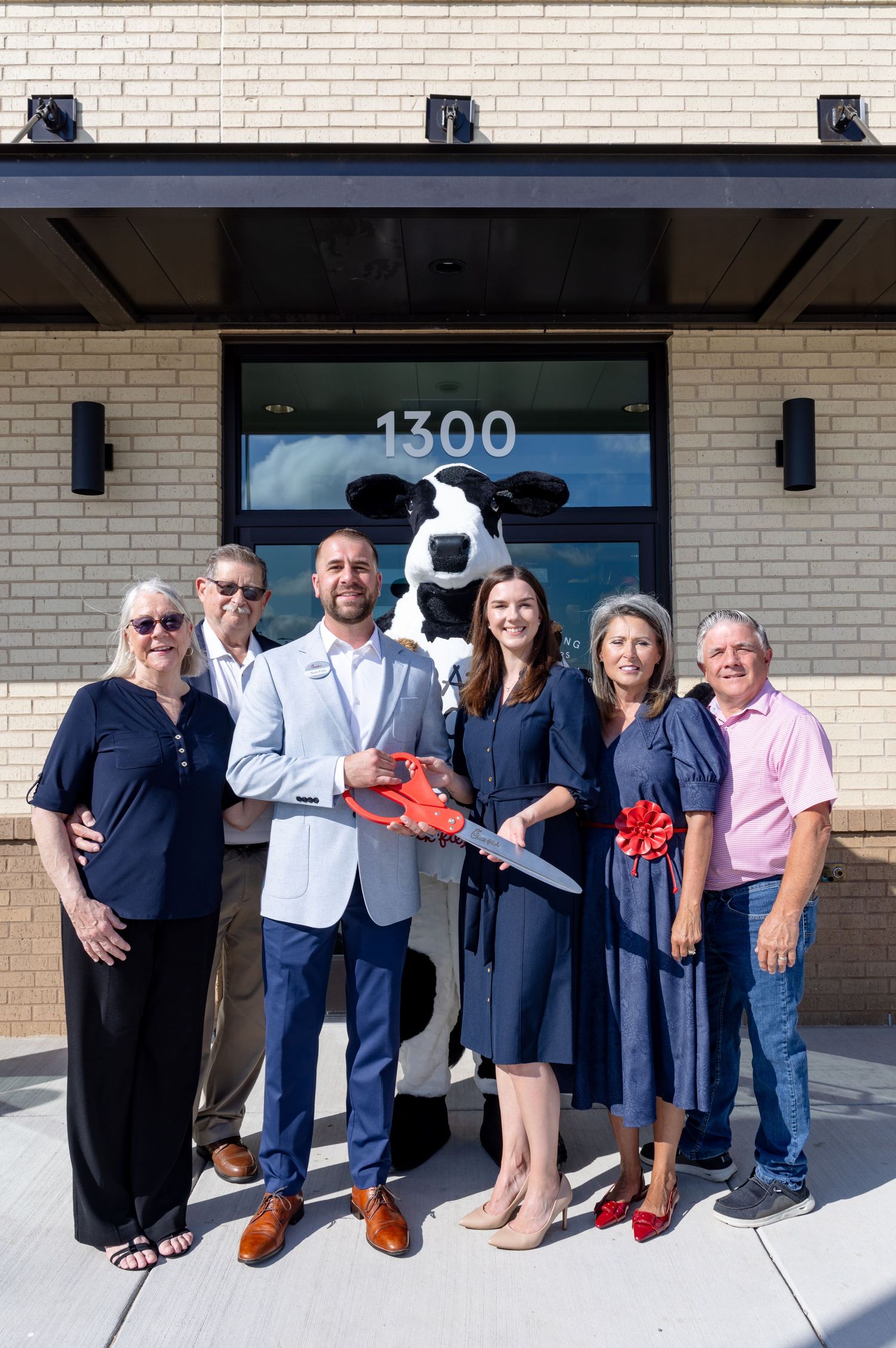 Group holding oversized key with Chick-fil-A cow mascot at grand opening of location 1300.