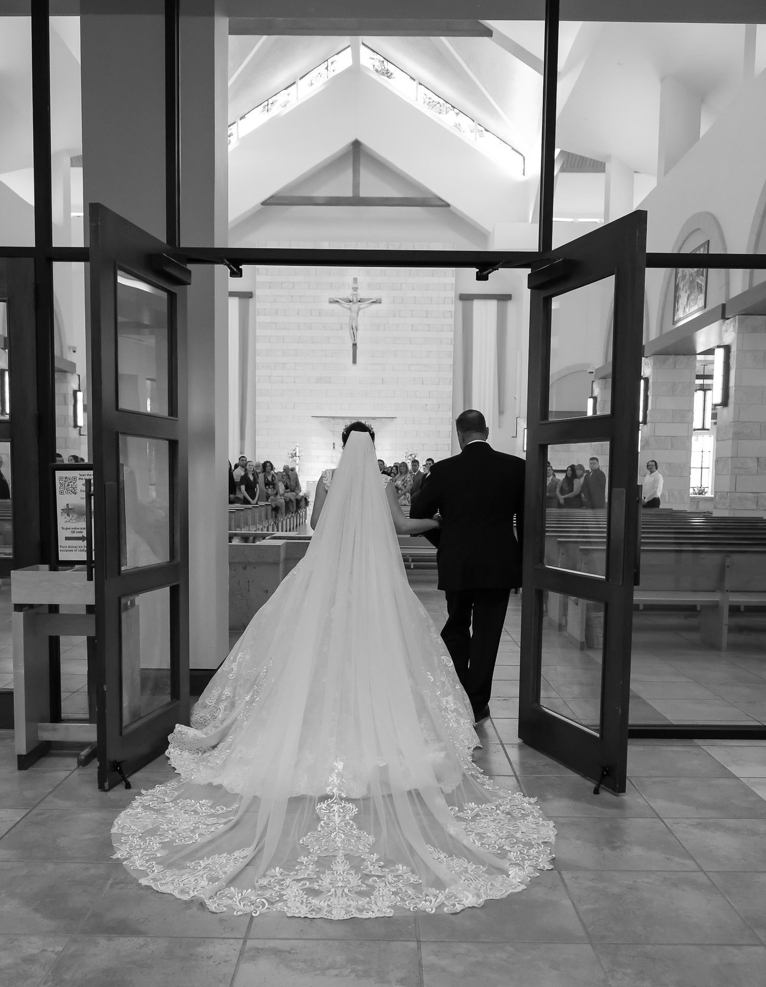 Black and white photo of bride with cathedral veil entering catholic church with dad.
