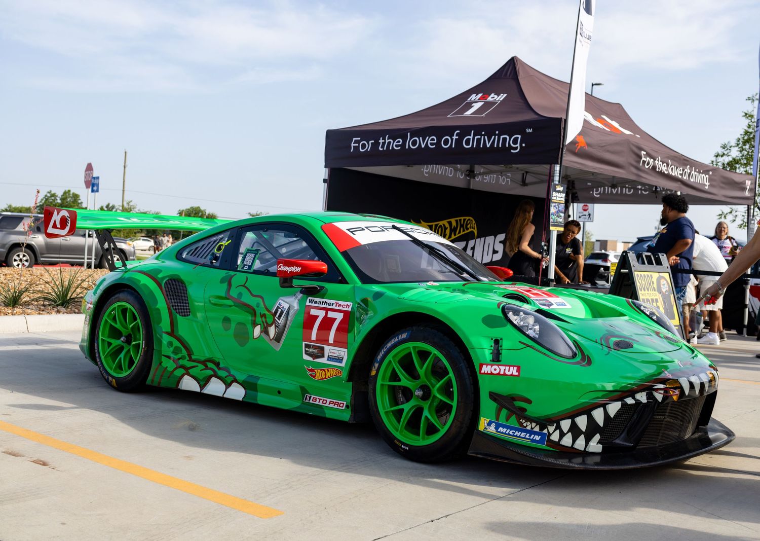 Green Porsche 911 GT3 race car #77 with shark teeth design on display at motorsport event.