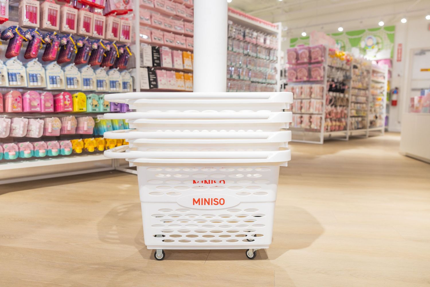 White MINISO branded shopping baskets stacked on wheels in a brightly lit retail store aisle.