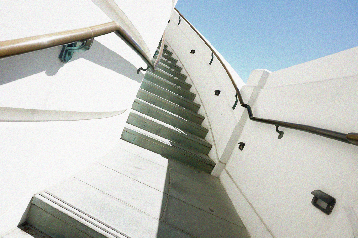 Low-angle view of white modern outdoor staircase with metal railings against a bright blue sky.