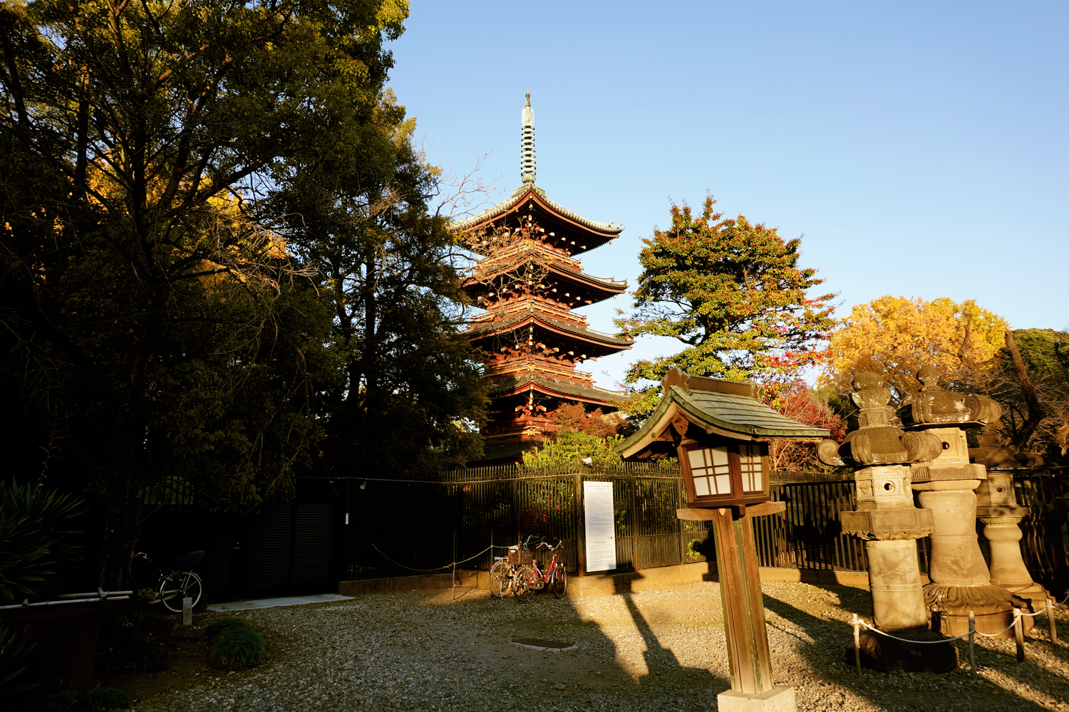 A five-story Japanese pagoda rises above stone lanterns and autumn trees in a peaceful temple garden.