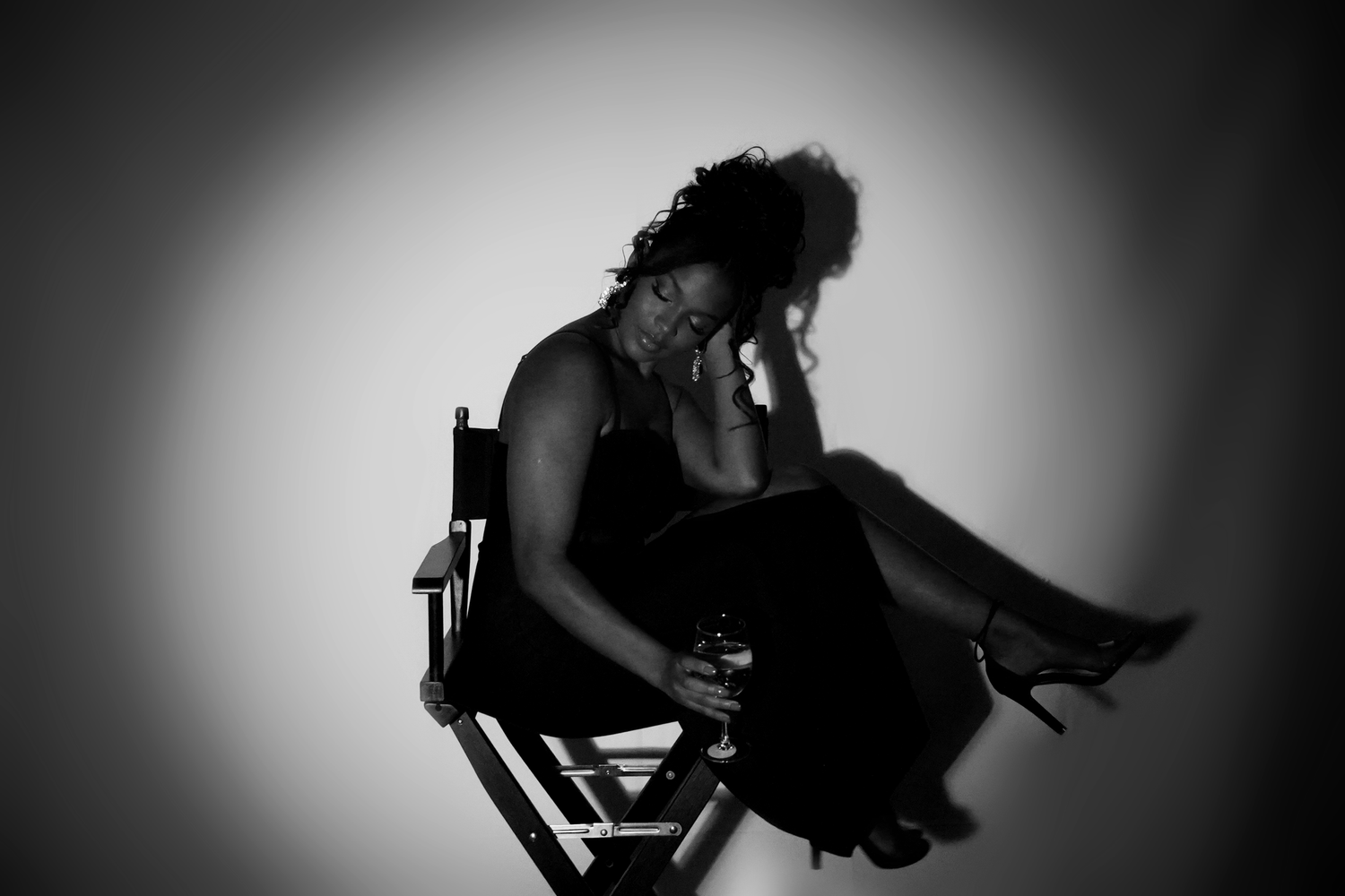 Black and white photo of a woman sitting on directors chair with head in hands in emotional pose.