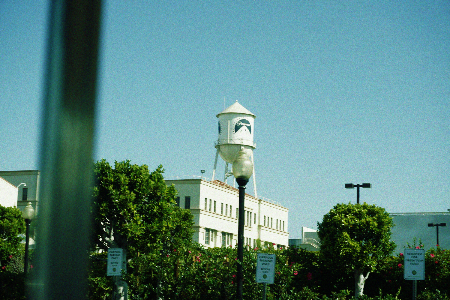 Historic white clock tower building surrounded by lush green trees under a bright blue sky.