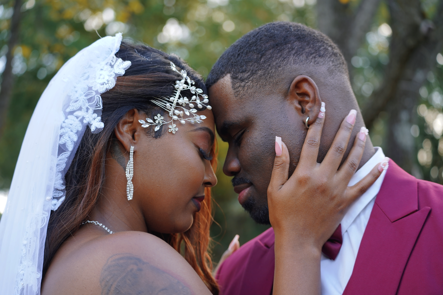 Romantic close-up of newlywed couple touching foreheads tenderly, bride in floral veil and groom in red suit.