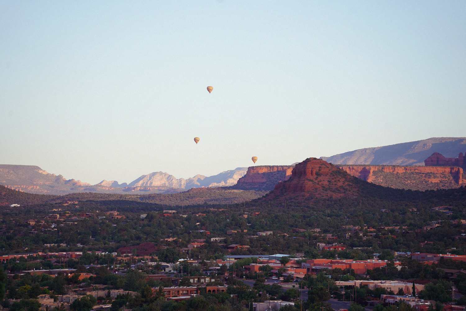 Hot air balloons float over Sedona Arizona red rock landscape at sunset with city below.