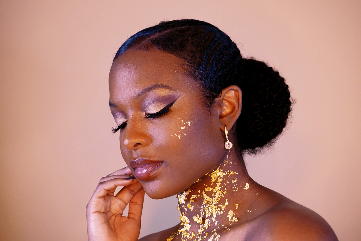 Black woman with gold foil neck makeup and pearl earring in a beauty portrait.