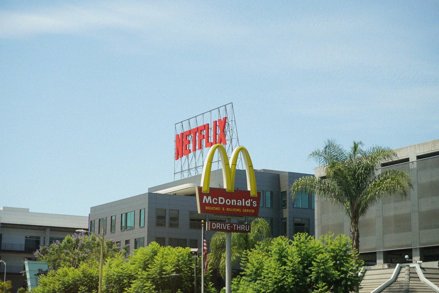 Netflix headquarters sign alongside a McDonald's golden arches billboard in Los Angeles on a sunny day.