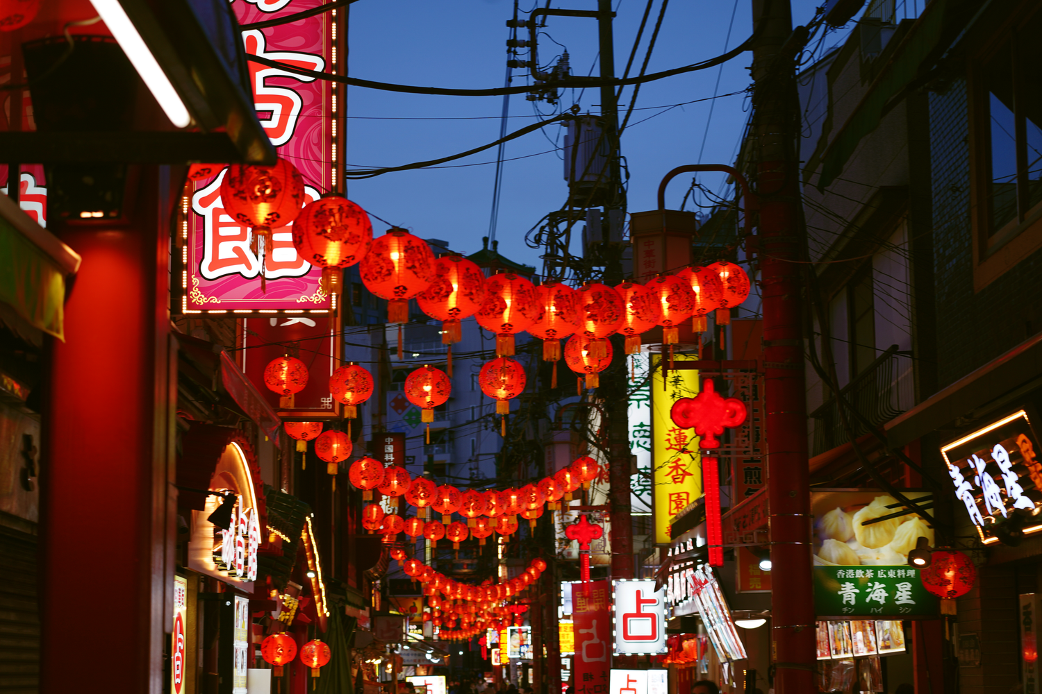 Vibrant red Chinese lanterns illuminating a bustling Chinatown street at night with neon signs.