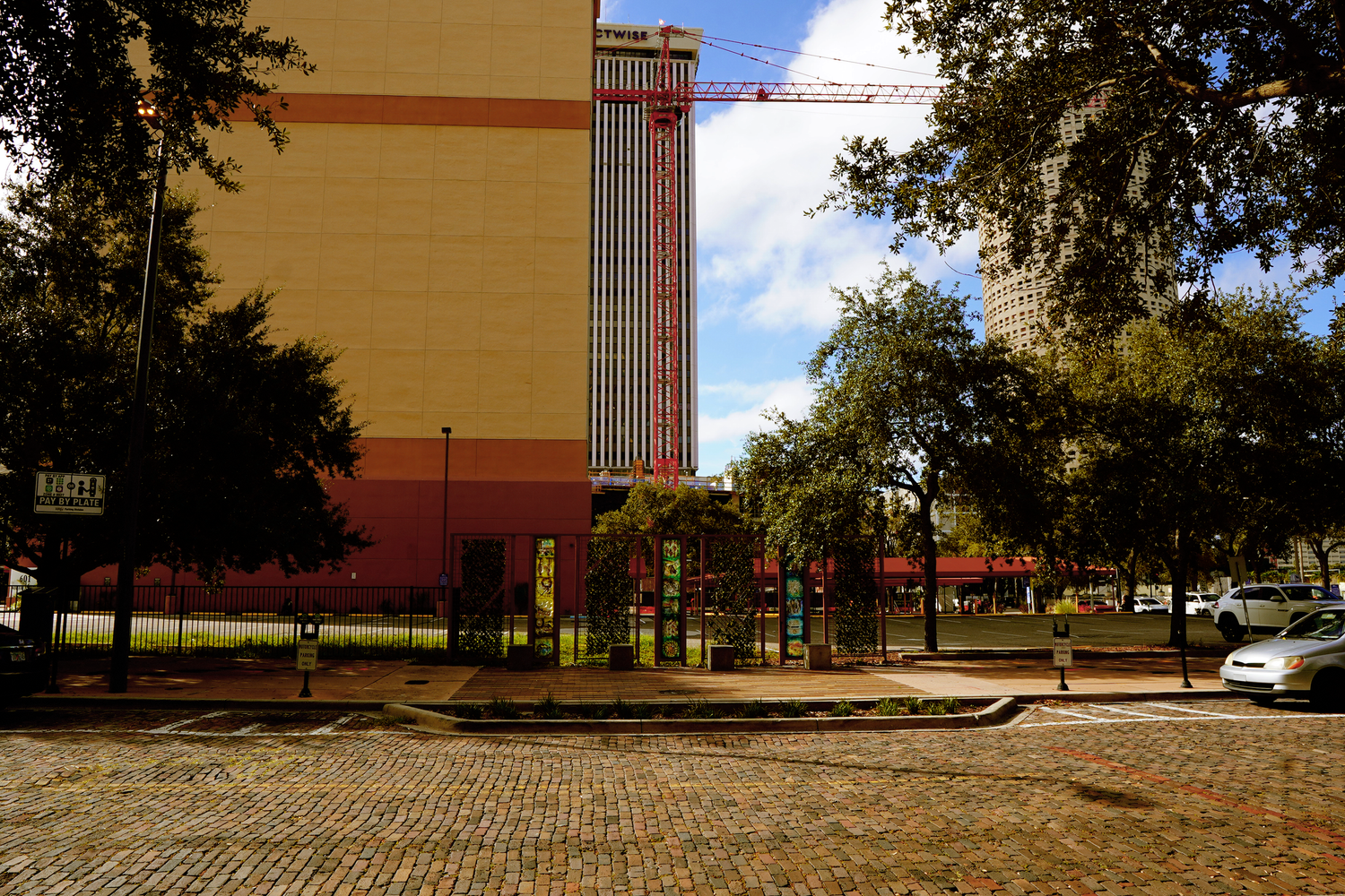 A large yellow building facade with cobblestone street and oak trees in an urban Tampa neighborhood.