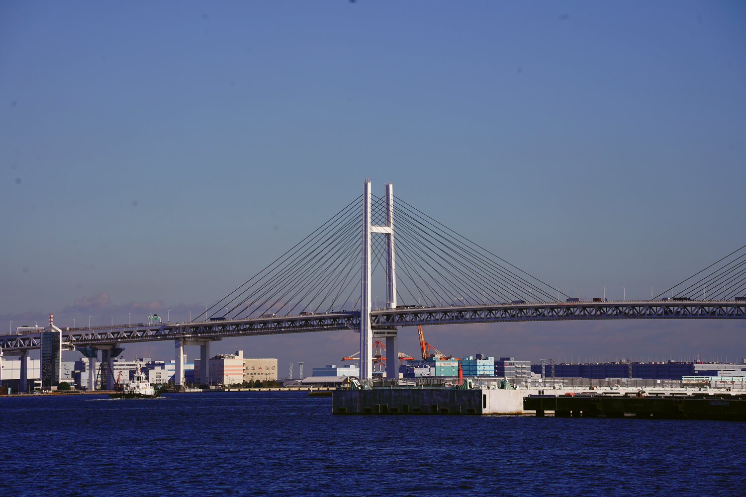 Yokohama Bay Bridge spanning the harbor under a clear blue sky with city skyline in background.