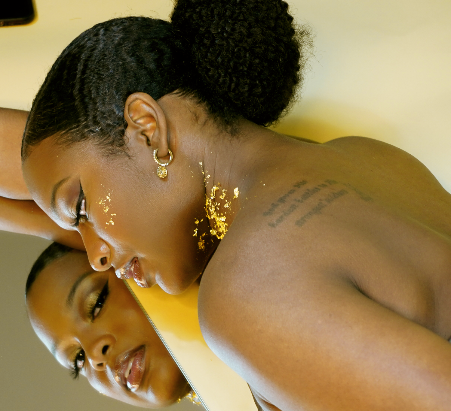 Black woman with natural hair wearing gold earrings and gold leaf makeup in artistic portrait.