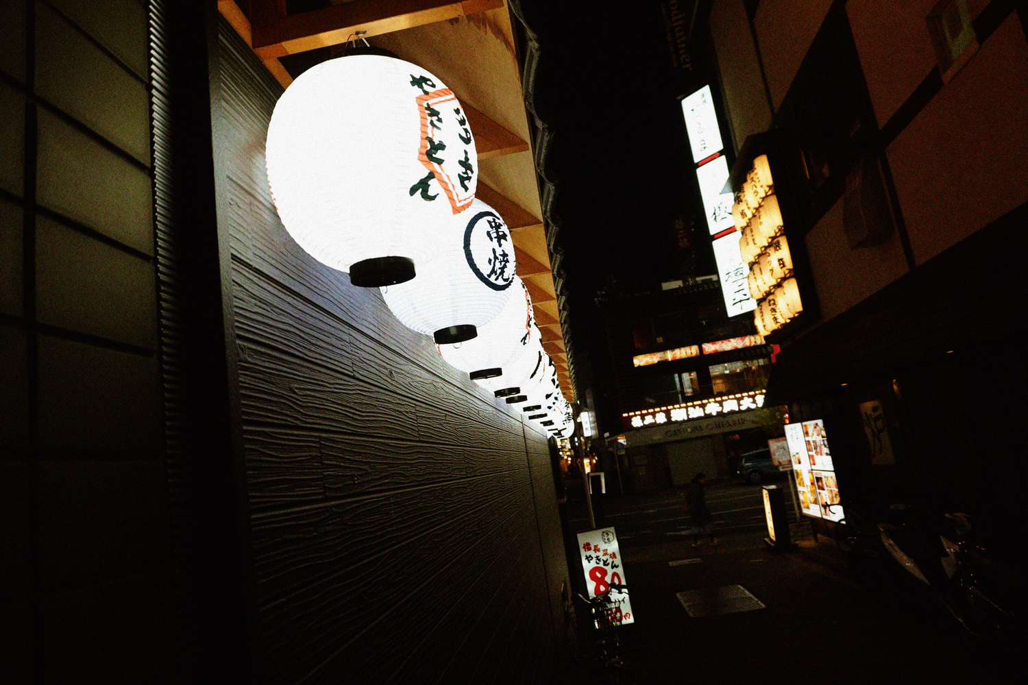 Glowing Japanese paper lantern illuminating a narrow alley at night.