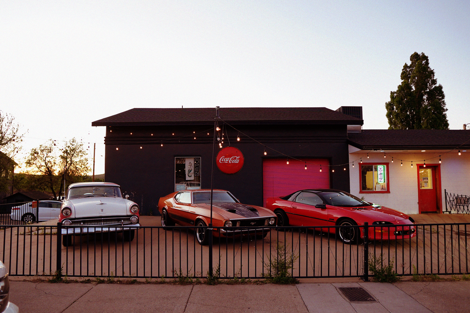 Classic vintage American muscle cars parked outside retro diner with Coca-Cola sign at dusk.