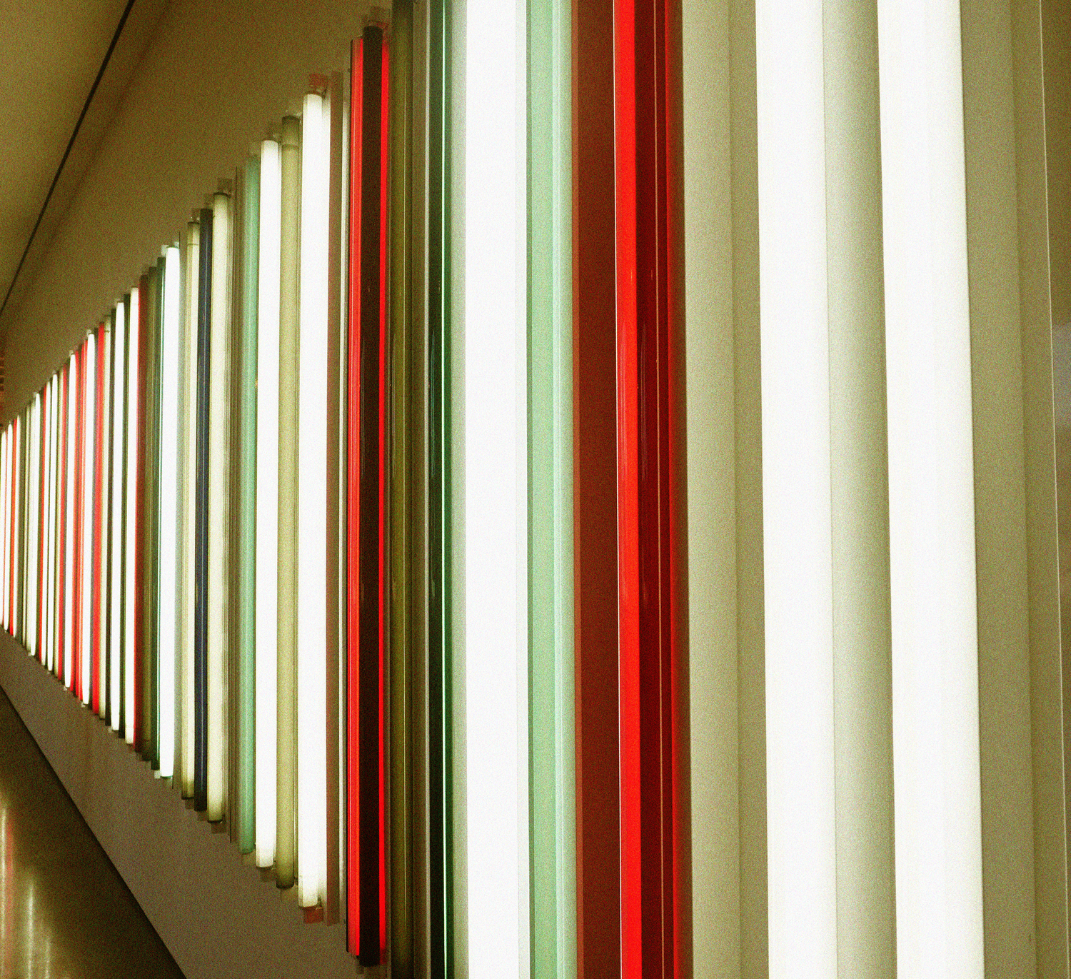 Modern interior wall installation featuring alternating red and white vertical neon light tubes in a corridor.