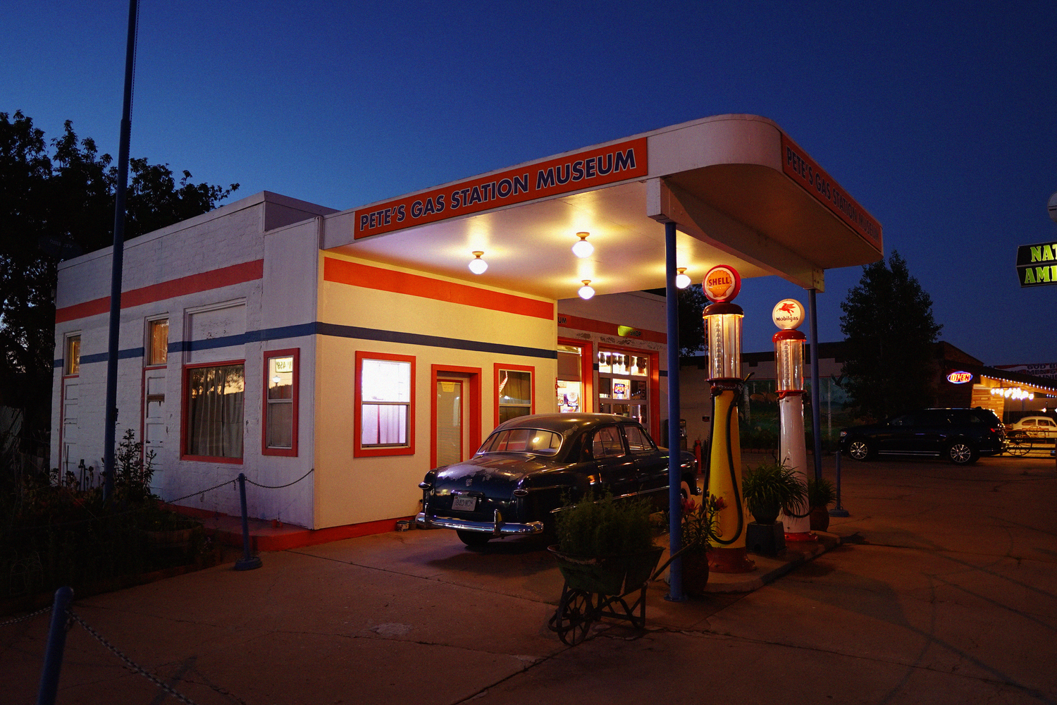 Vintage Route 66 gas station museum lit up at night with classic car parked outside.