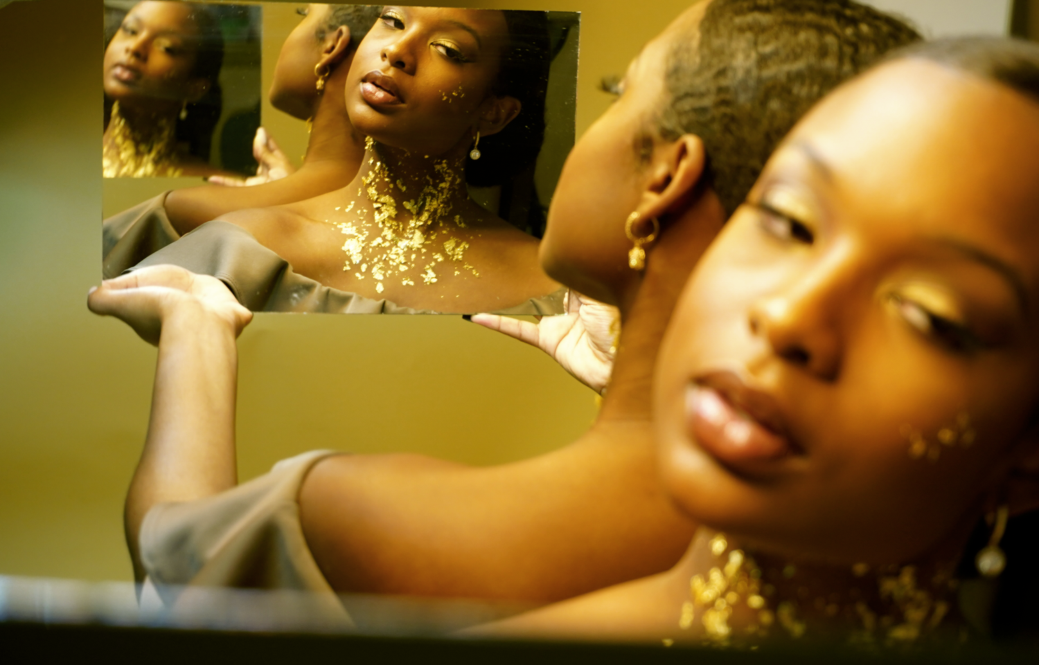 Black woman with gold foil makeup reflected in multiple mirrors.