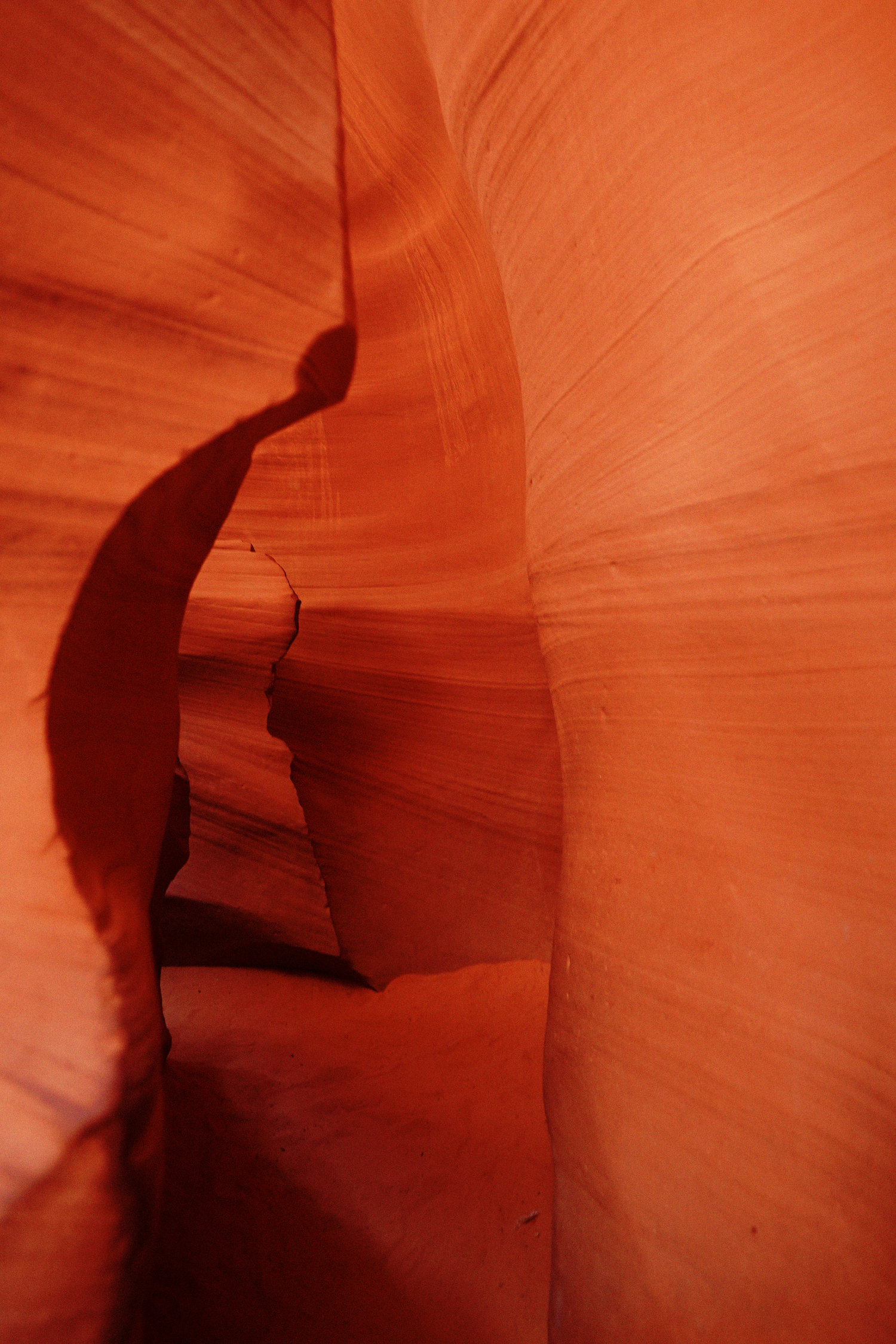 Narrow slot canyon passage with glowing orange-red sandstone walls and dramatic light and shadow.