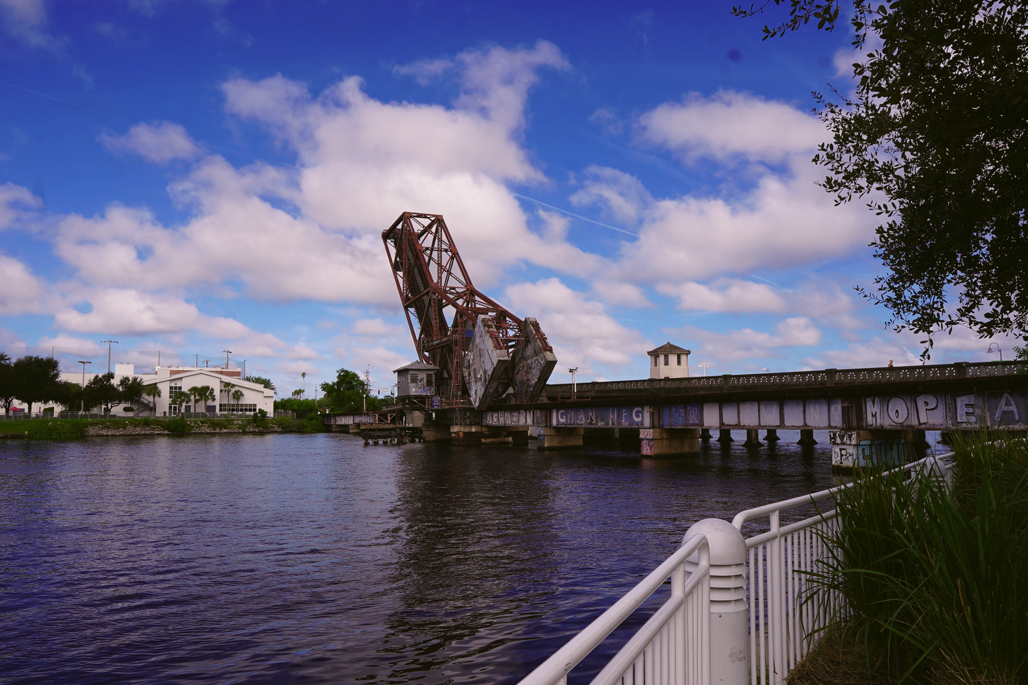 A historic raised drawbridge over the Hillsborough River in Tampa under a bright blue cloudy sky.