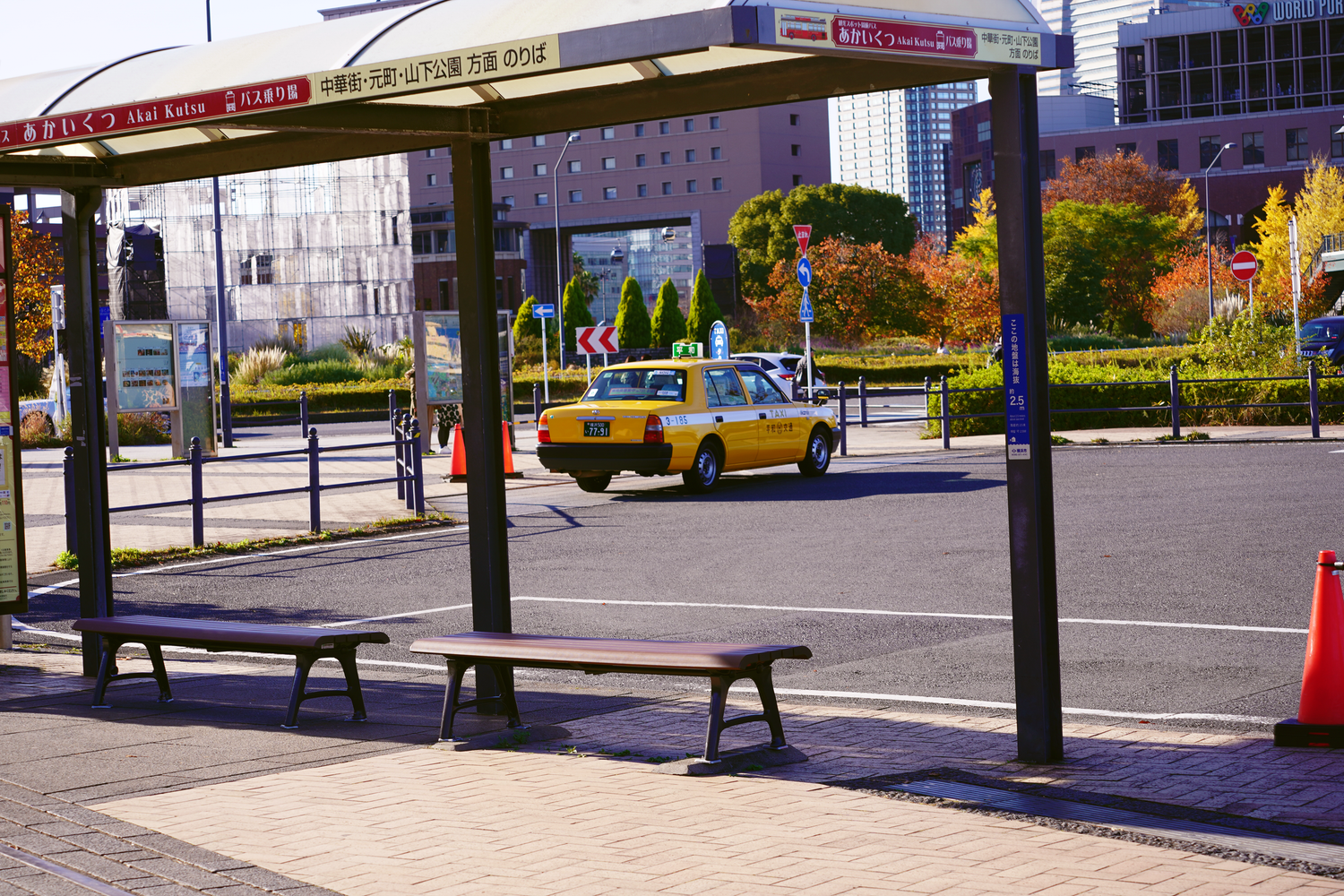 Yellow taxi cab parked near a modern bus stop shelter on a sunny urban street in Japan.