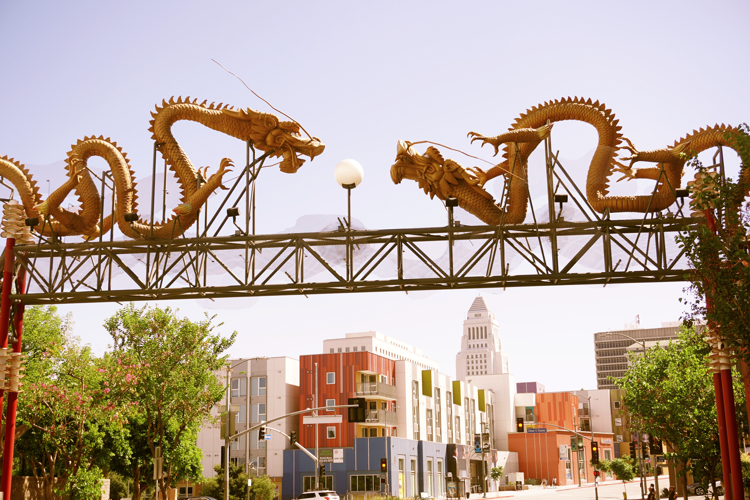 Golden dragon sculptures on an ornate gateway arch in Los Angeles Chinatown with city skyline in background.
