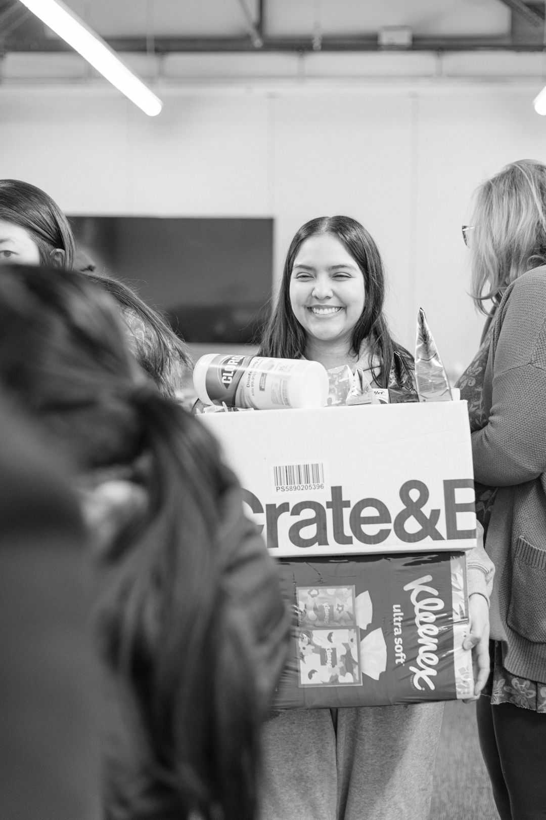 Black and white candid group photo showing people gathered around boxes and packages.