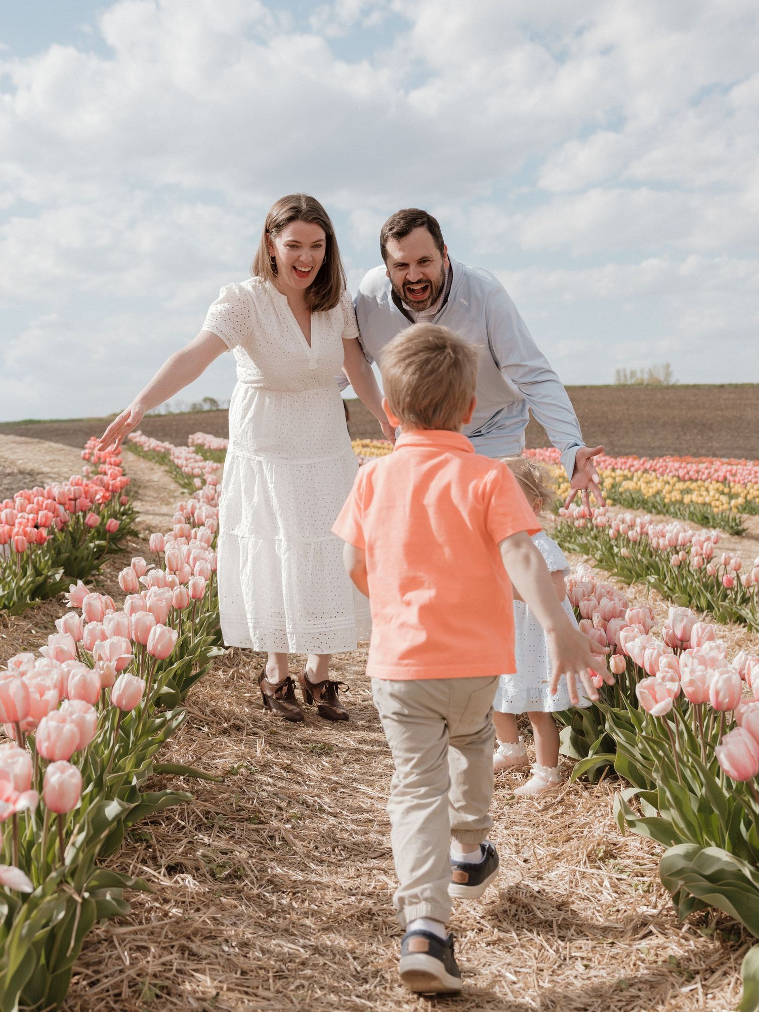 Family laughing together in a vibrant pink tulip field on a sunny spring day.