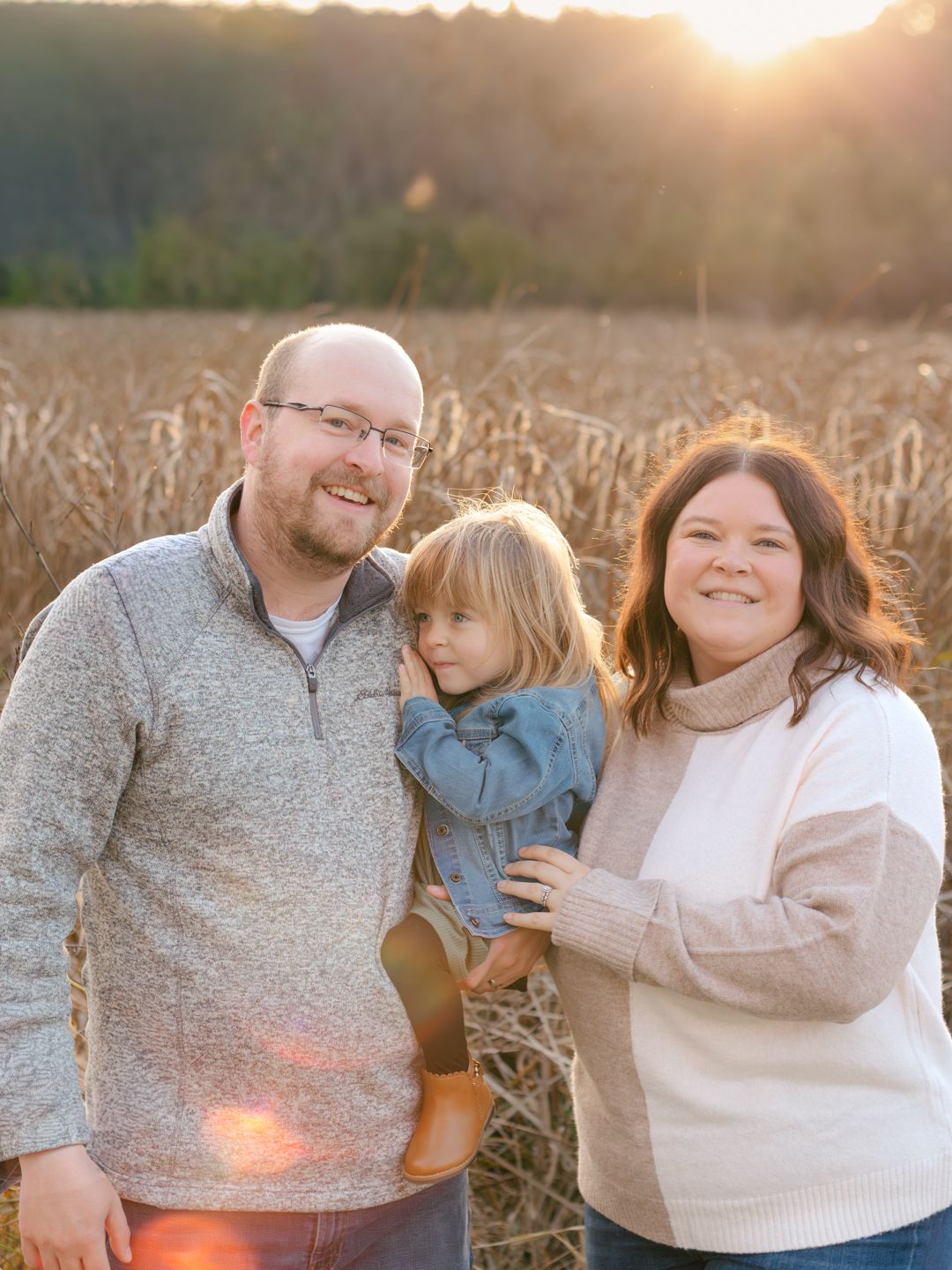 Family shares warm embraces during golden hour photoshoot in autumn field.
