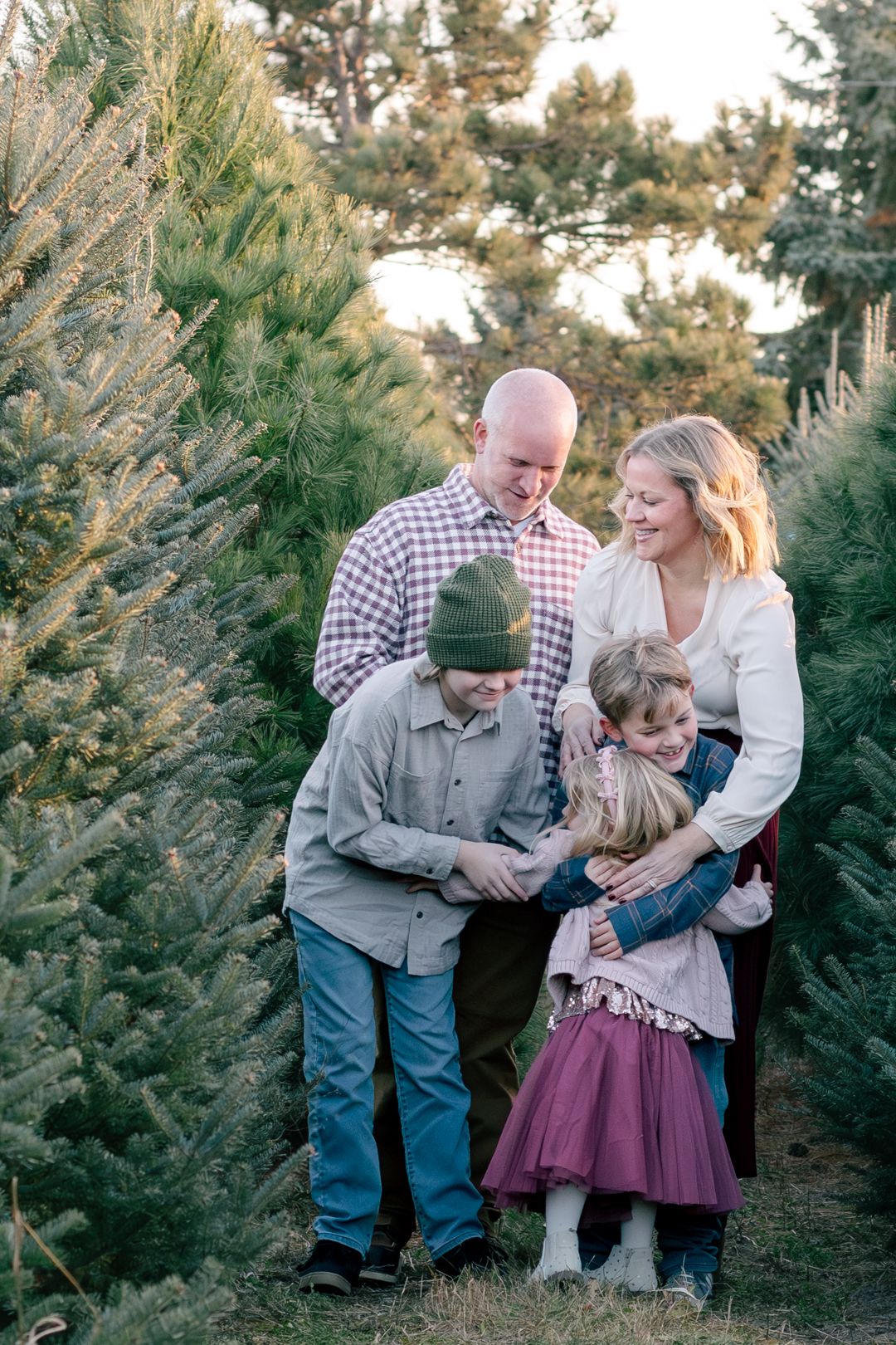 Family shares joyful moments together among evergreen trees during a winter photo session.