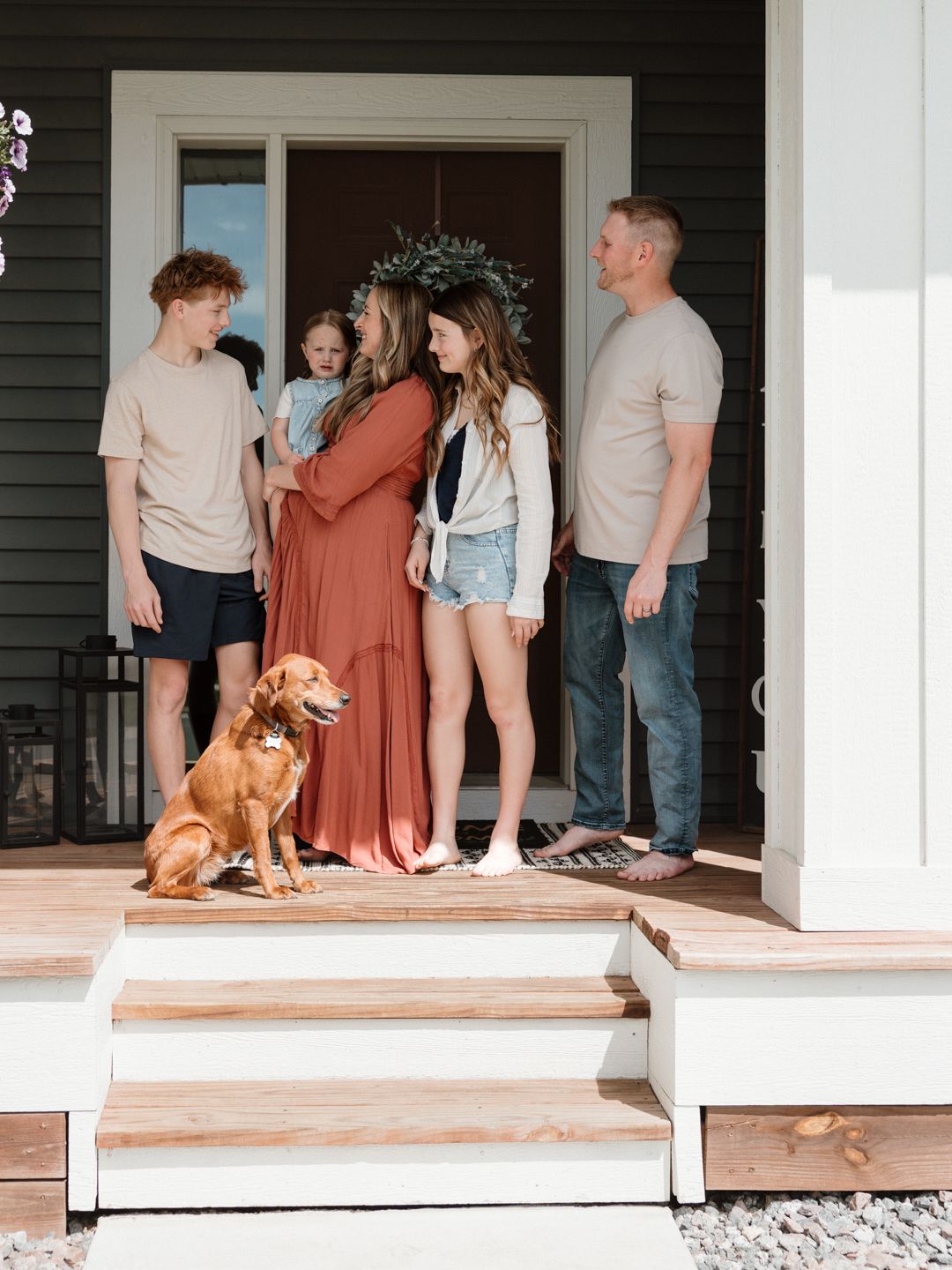 Family gathering on wooden porch steps with golden dog, mom in rust maxi dress, relaxed outdoor photo.